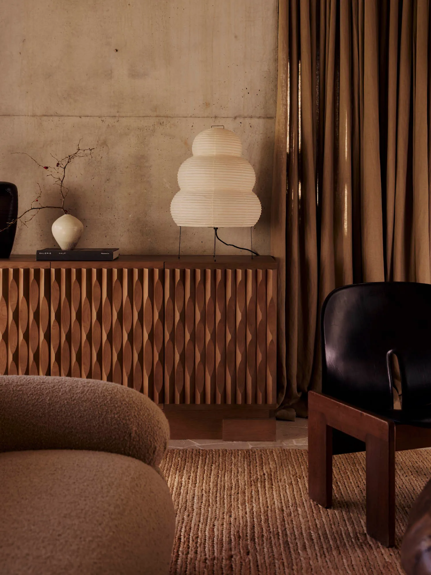 Cozy living room with a brown sofa, black chair, and a potted plant, set on a rug, with a table and lamp, in a well-lit space