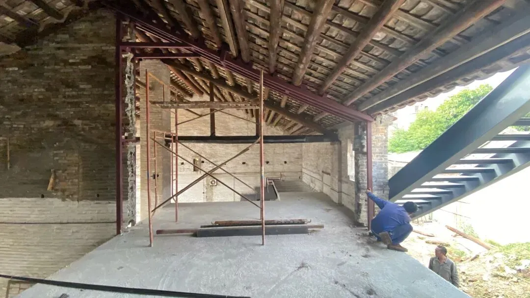 A man kneeling on a dirt floor in a construction site with a metal beam and cement floor, focused on his task