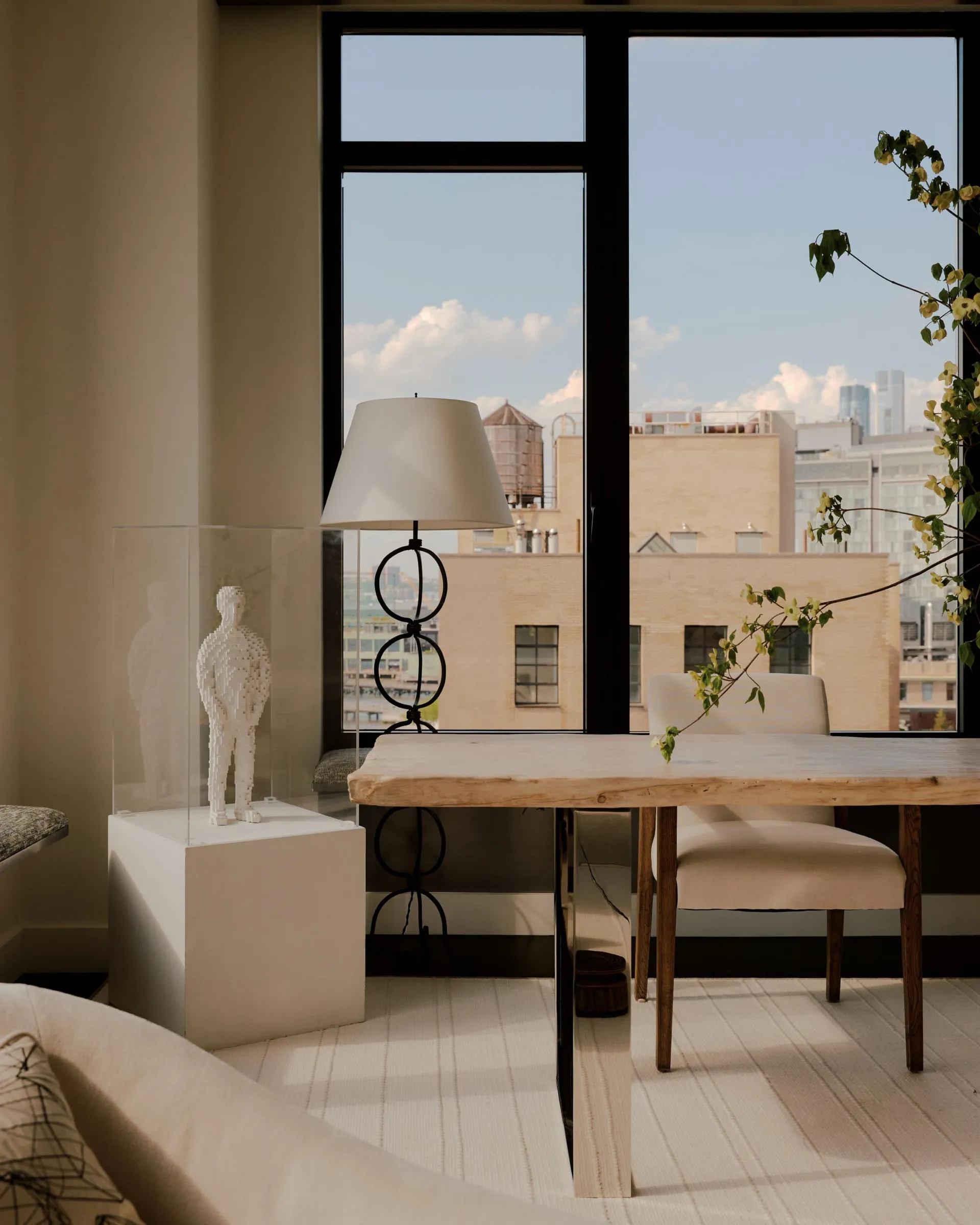 A well-lit living room with a white couch, a chair, a dining table, and a lamp, surrounded by wood and glass materials