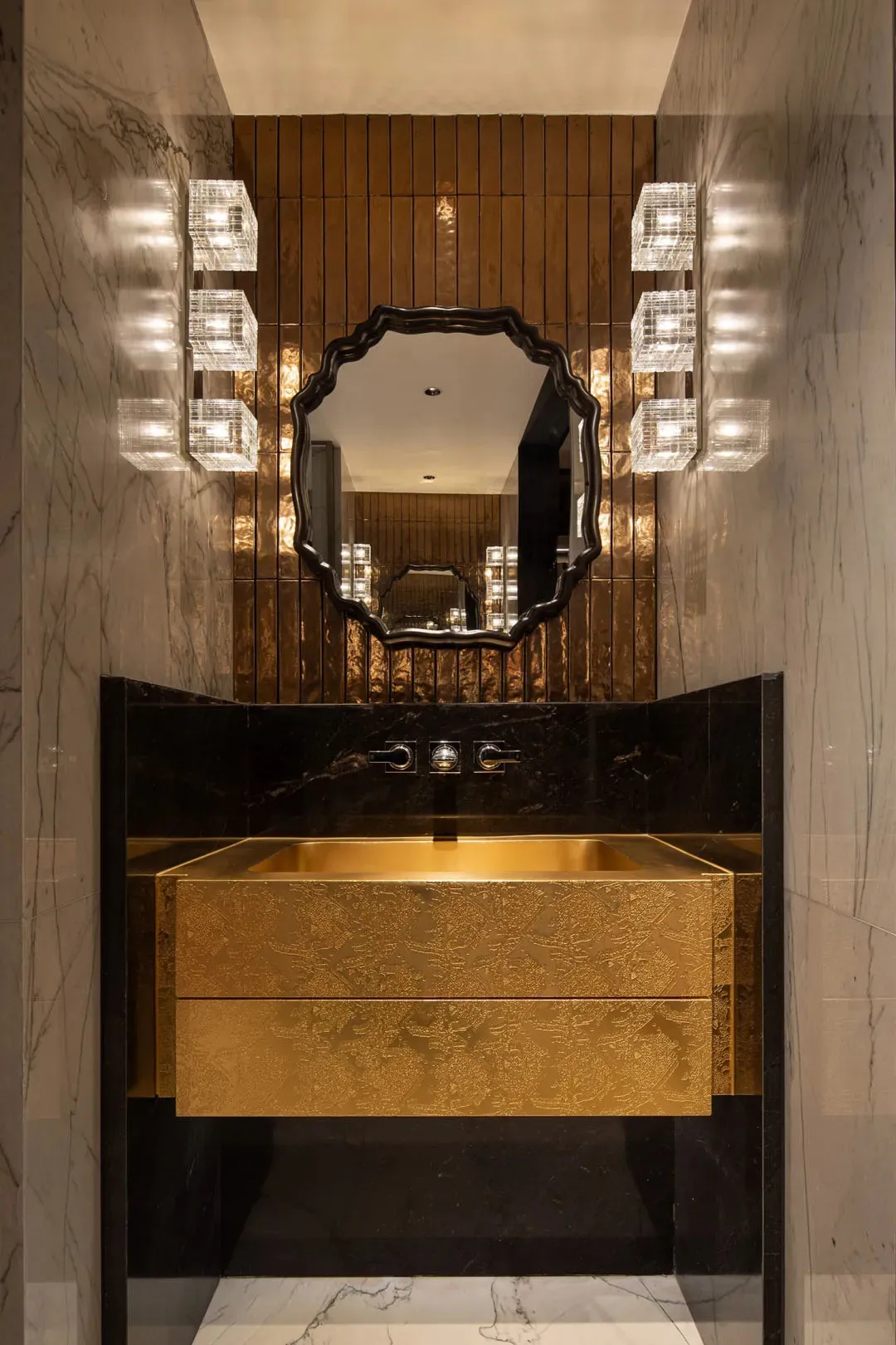 Modern bathroom with a gold-toned sink, mirror, and drawer, set against a black countertop, in a well-lit space with a warm and inviting atmosphere