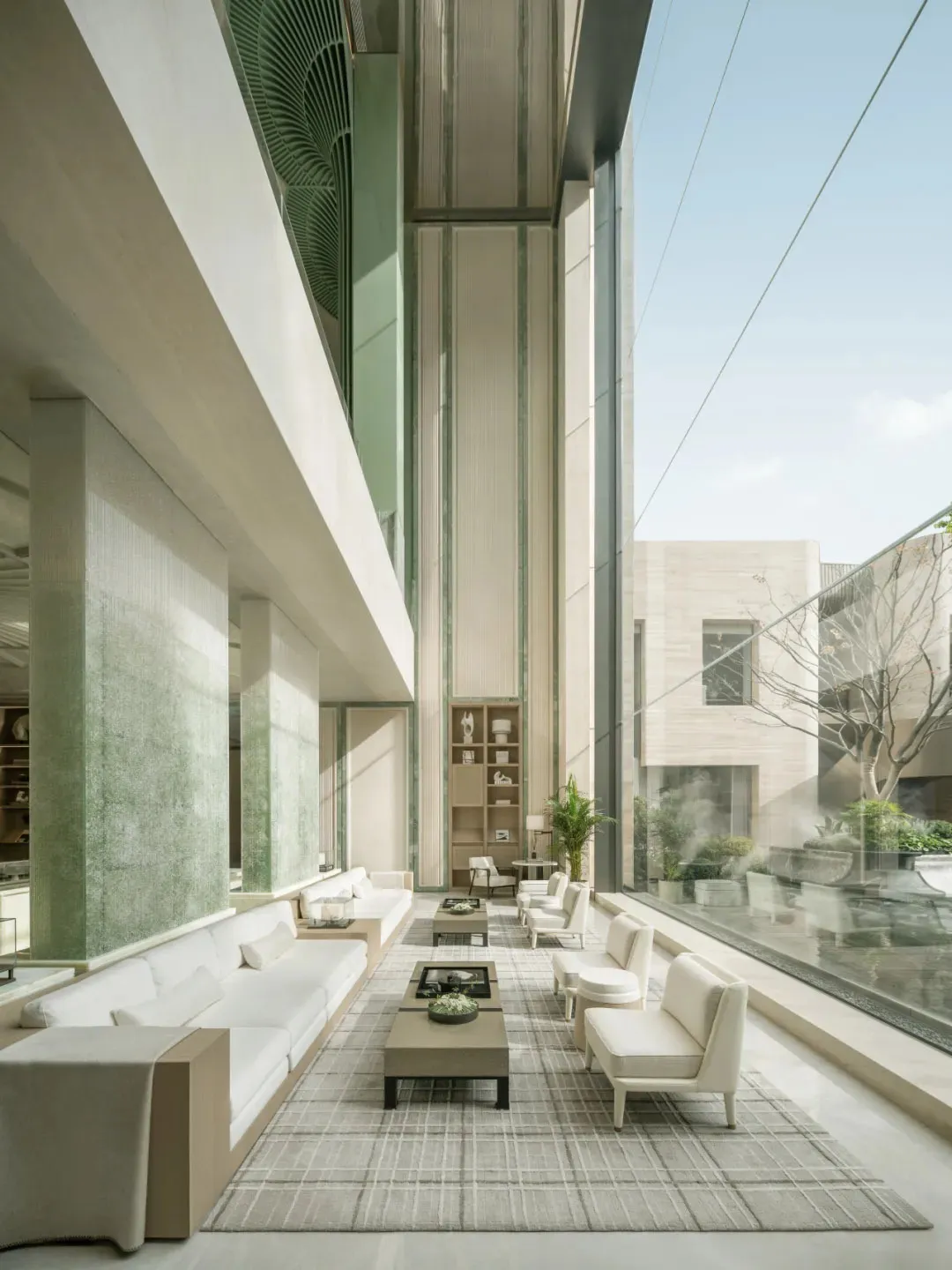 Large open living room with glass wall, furniture, potted plants, and vases, filled with natural light