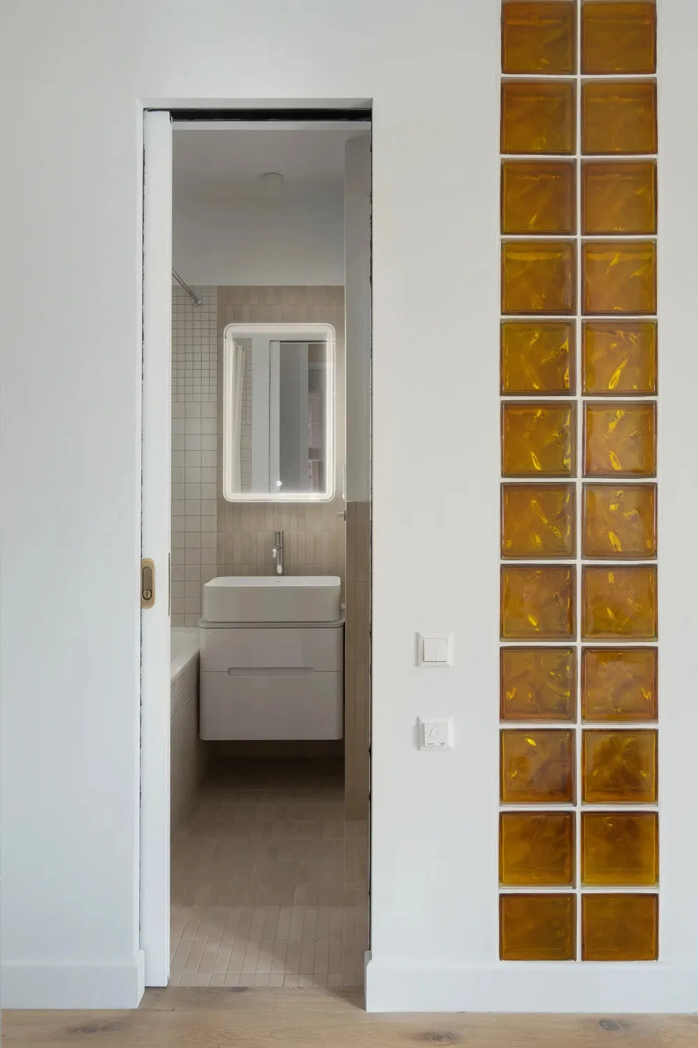 Bathroom with a white sink, mirror, and toilet, set against a tiled background with dim lighting