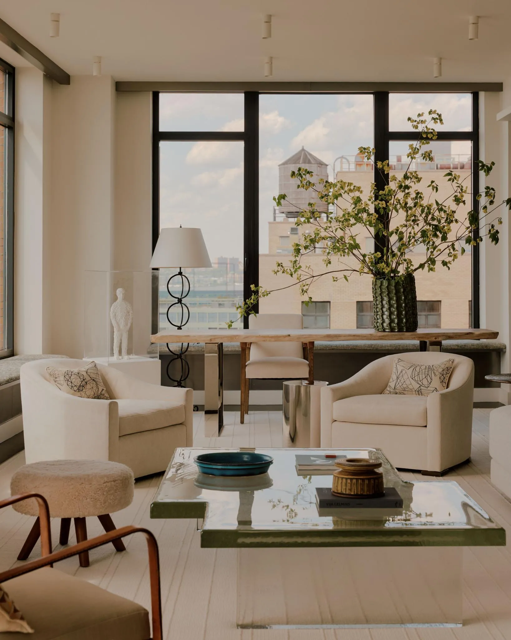 Cozy living room with a large window, a couch, chairs, and a dining table, surrounded by a potted plant, in a well-lit space