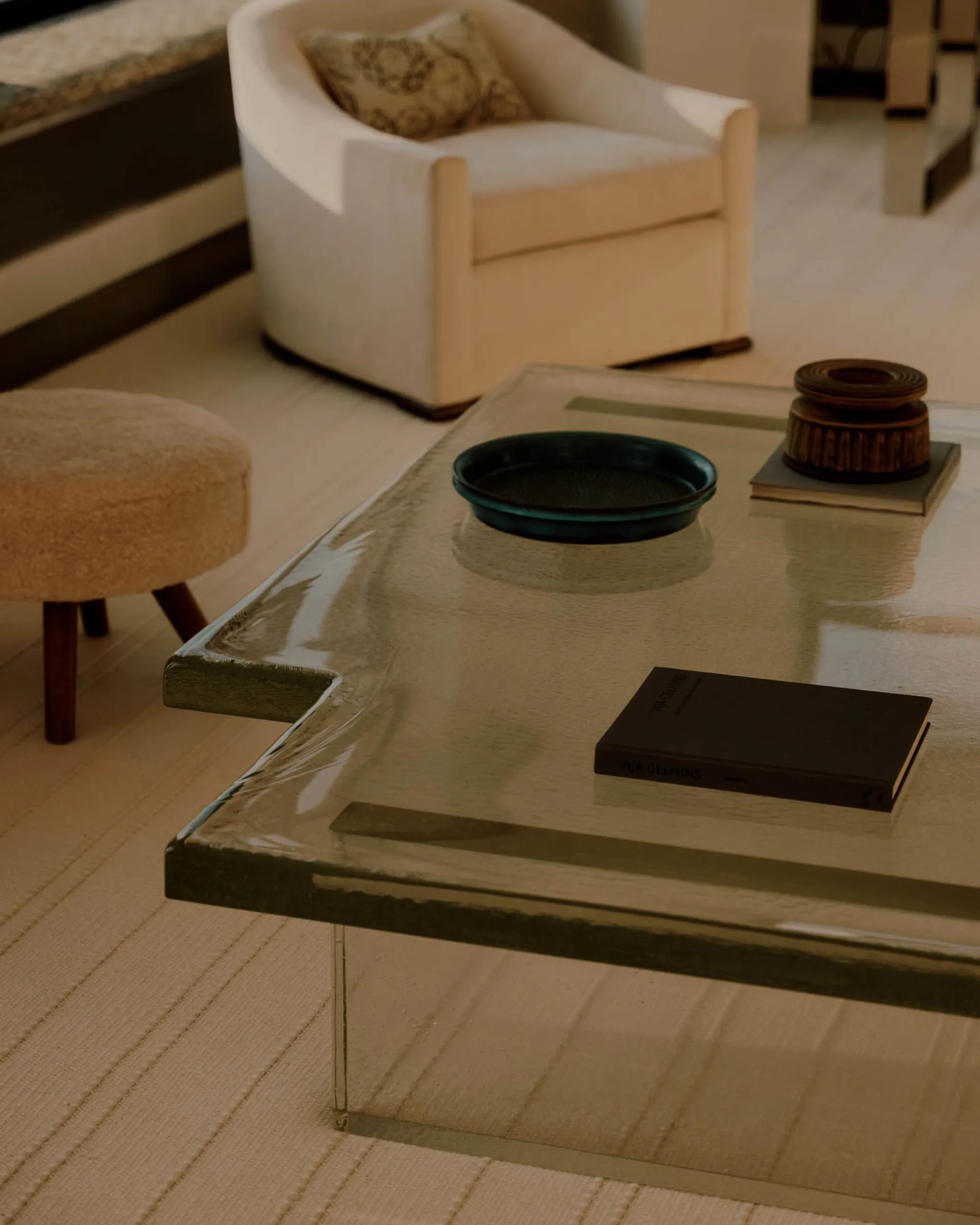 A well-lit living room with a glass coffee table, a couch, a chair, and a book, creating a cozy atmosphere