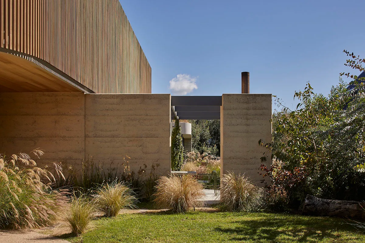 A modern house with a concrete exterior, a large window, and a patio area surrounded by greenery