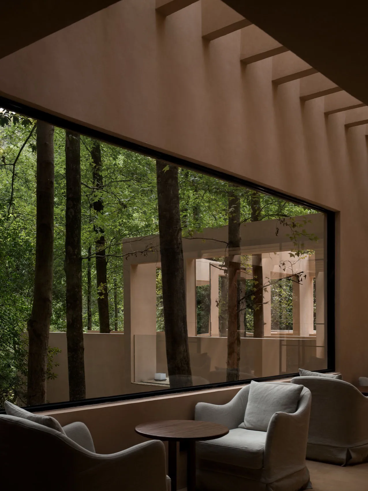 Cozy living room with a couch, chair, and dining table, surrounded by a forest view through a large window