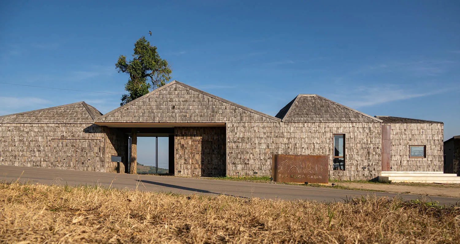 Photograph of a rustic cabin with a wooden exterior, featuring a unique design with a sloping roof and a cozy atmosphere