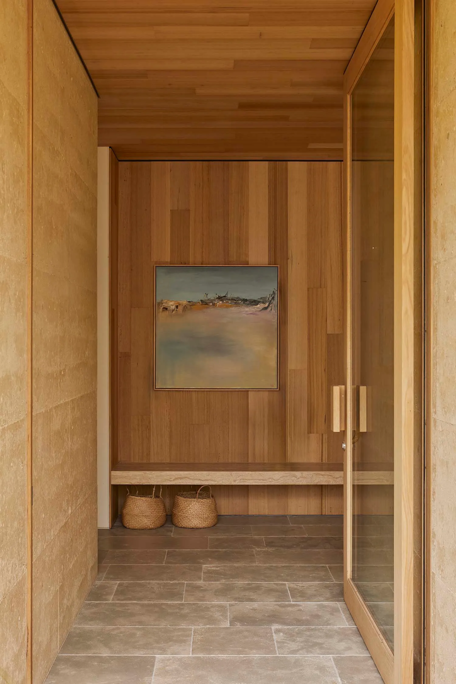 A modern bathroom with a wooden door and a beach scene painting on the wall, featuring a bench and a doorway, with dim lighting creating a cozy atmosphere