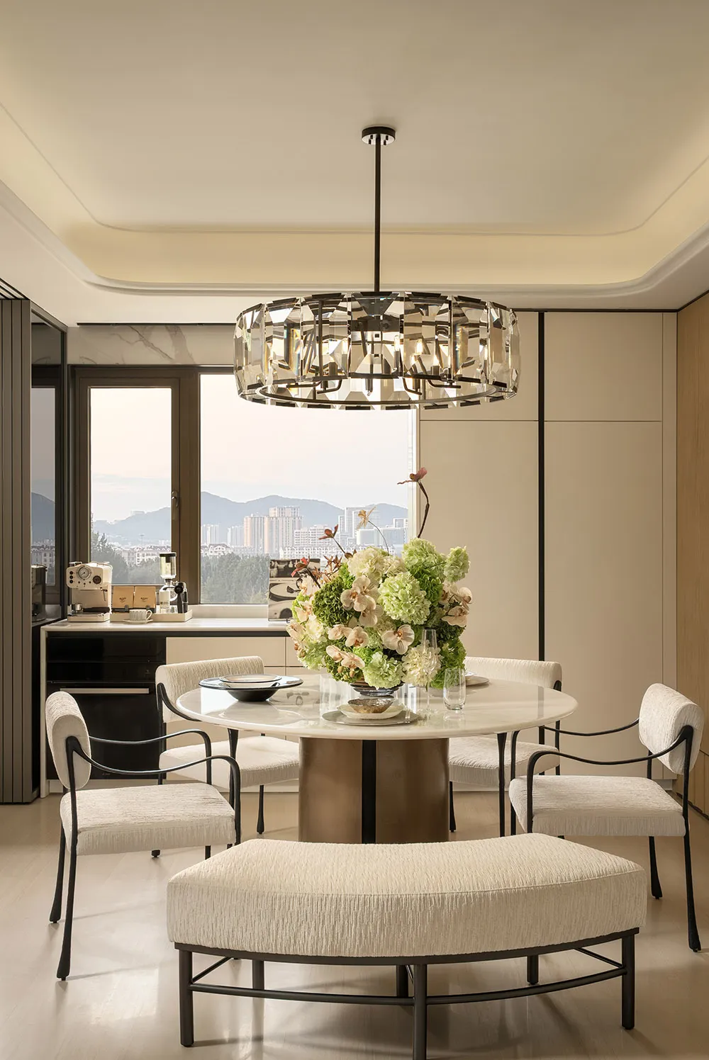 Dining room with a round table surrounded by chairs, a vase with flowers, and a modern style, with natural lighting creating a warm and inviting atmosphere