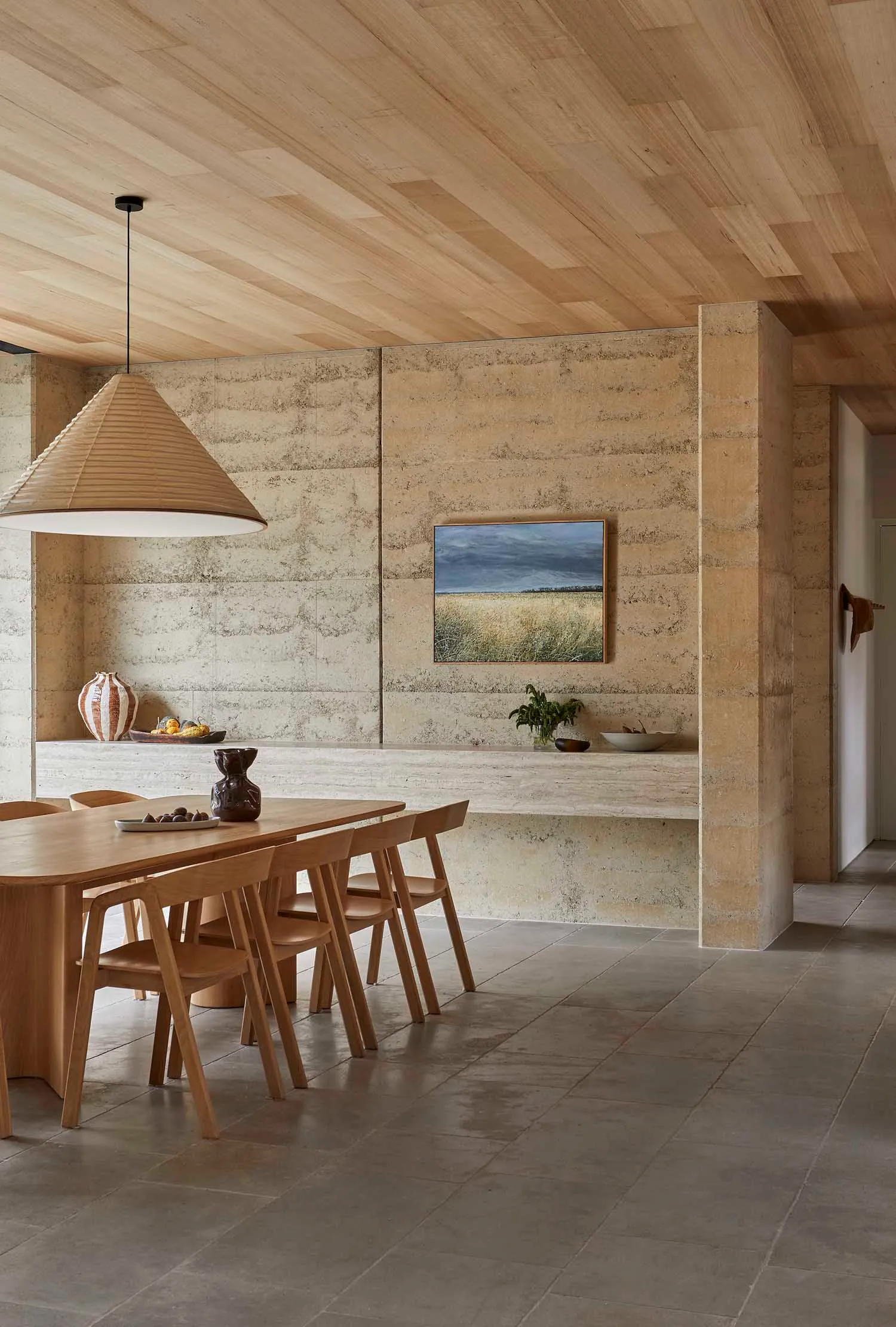 A modern kitchen with a dining table and chairs, surrounded by a counter with a vase, featuring wood and stone materials in a well-lit space