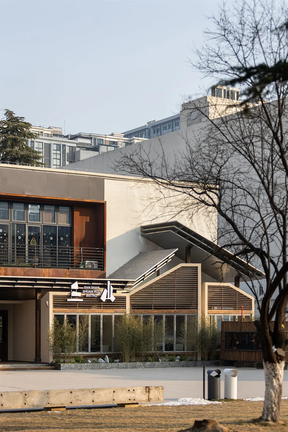 A modern building with a large white concrete wall and a tree in front, creating a calm and serene atmosphere