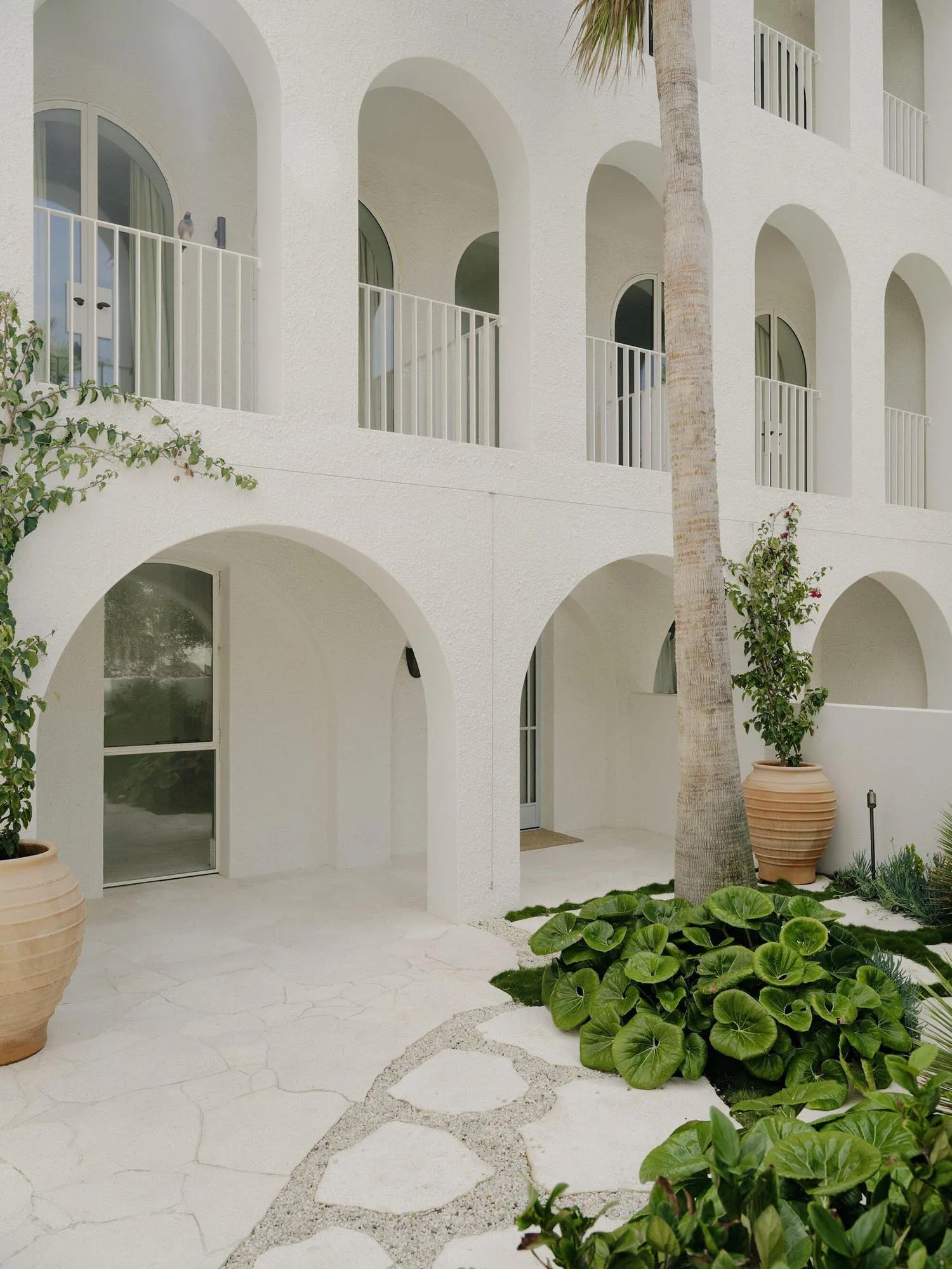 A modern hotel entrance with a large archway and row of arches, featuring a white building with a balcony and natural light streaming through the arches