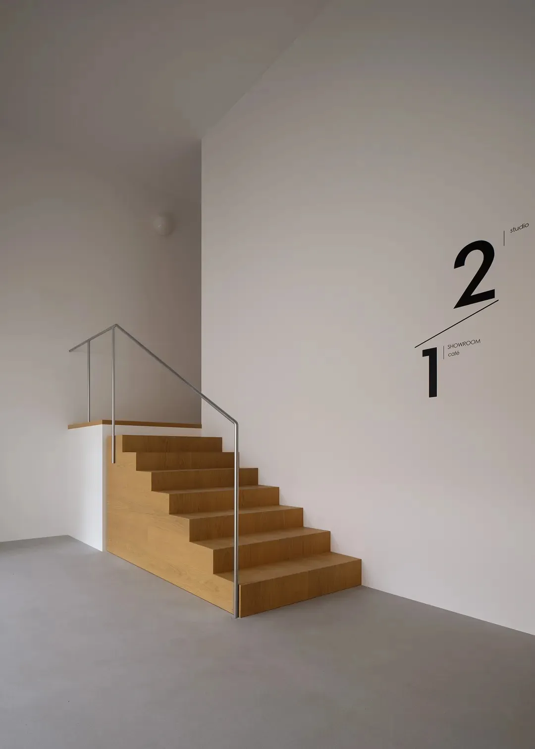 A dimly lit room with a minimalist wooden staircase and metal railing, featuring a white wall with a number 2