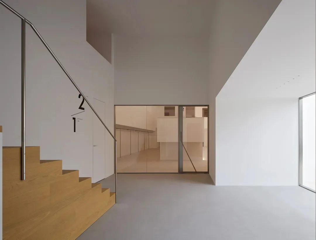A large, dimly lit room with a modern design, featuring a wooden staircase and metal railing, with a clean and minimalist appearance