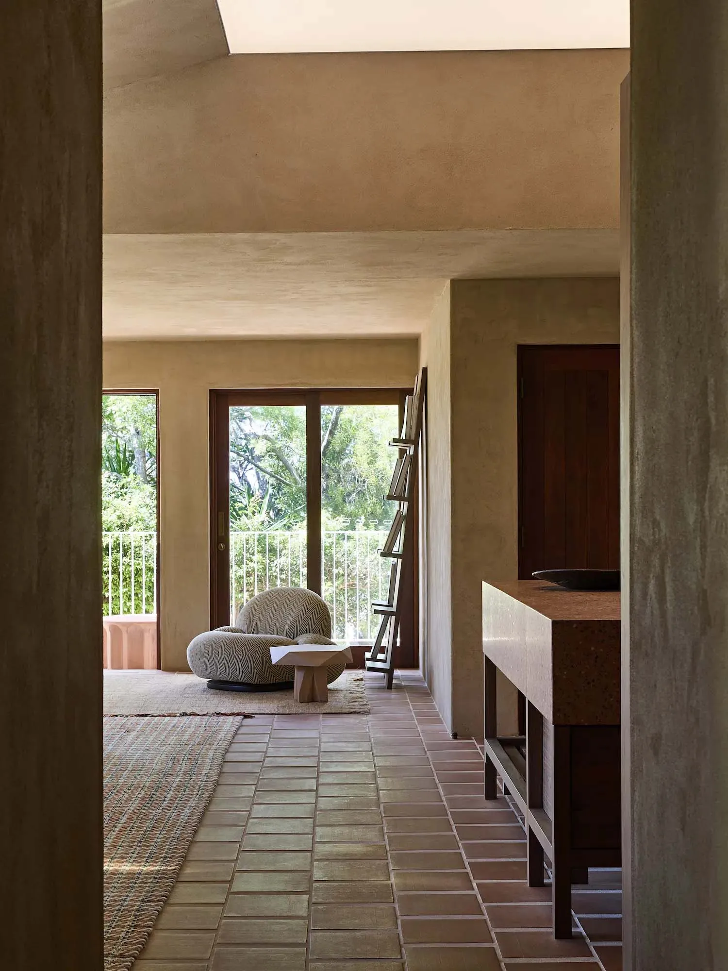 Cozy modern living space with a stone floor, a large window, and a stone wall, featuring a couch, chair, and dining table, with dim lighting and natural materials