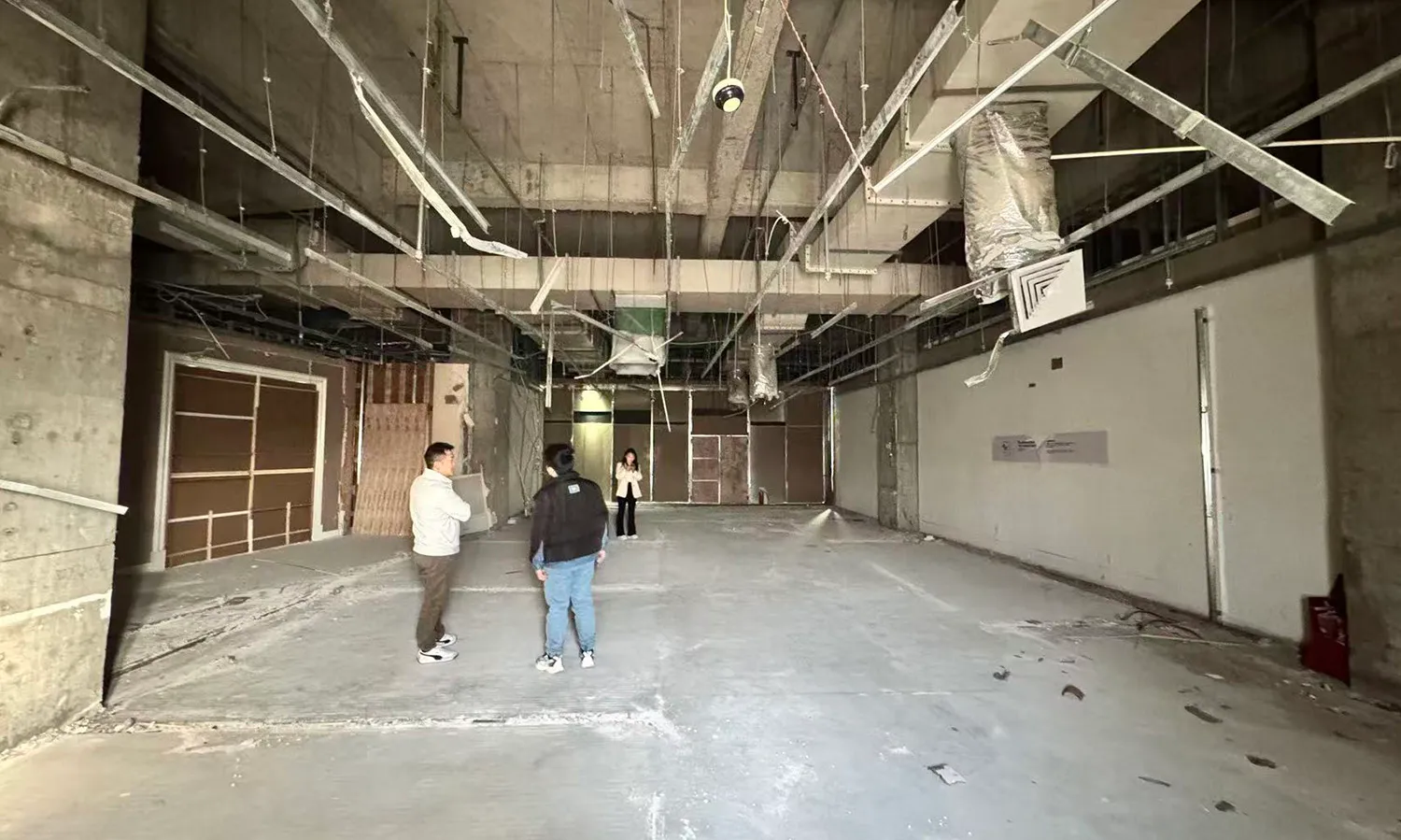 A large, empty room with a cement floor, a crane in the background, and a dim, moody atmosphere