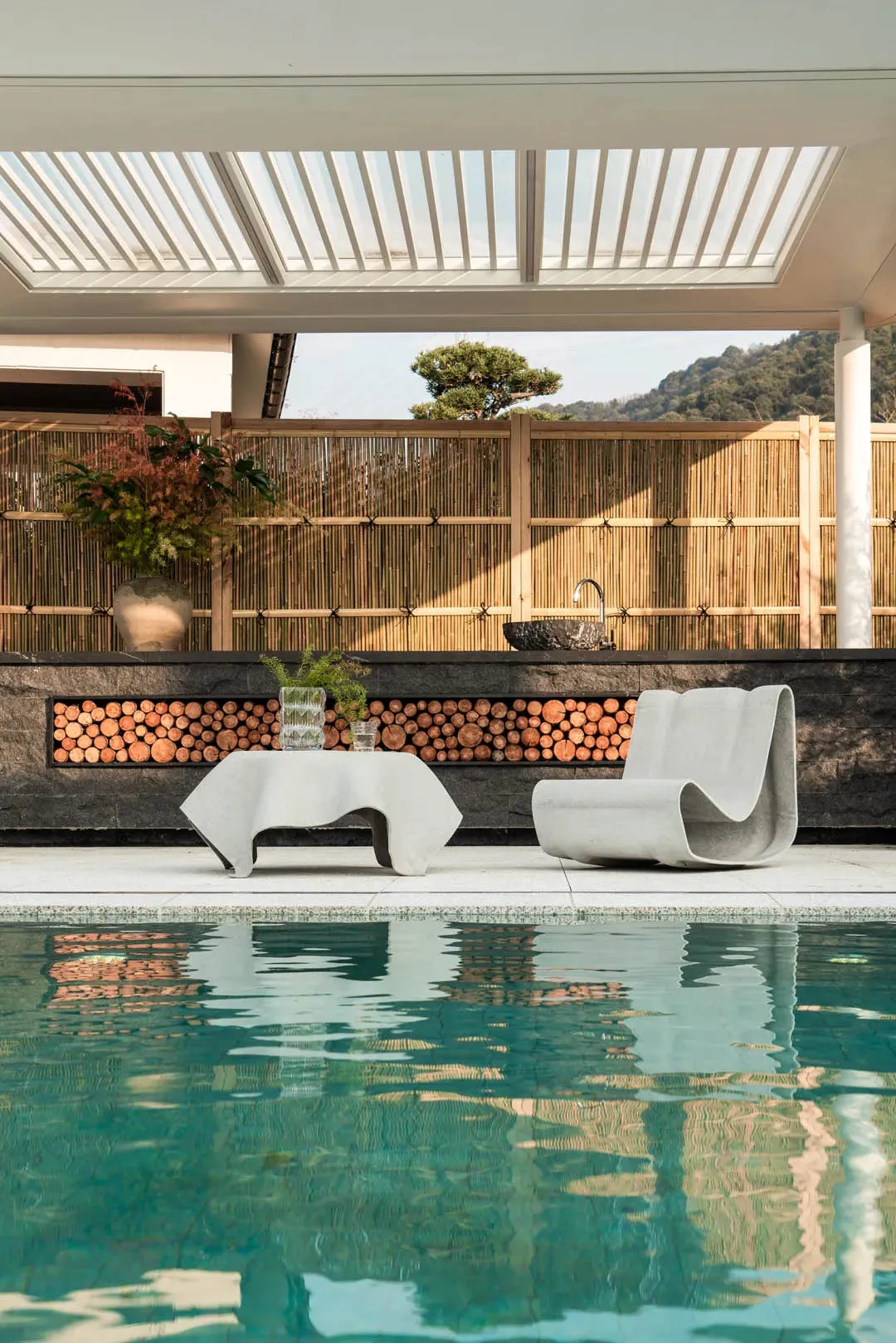 A pool area with a patio and a fence, surrounded by a deck and decorated with a potted plant and a vase, with natural sunlight creating a warm atmosphere