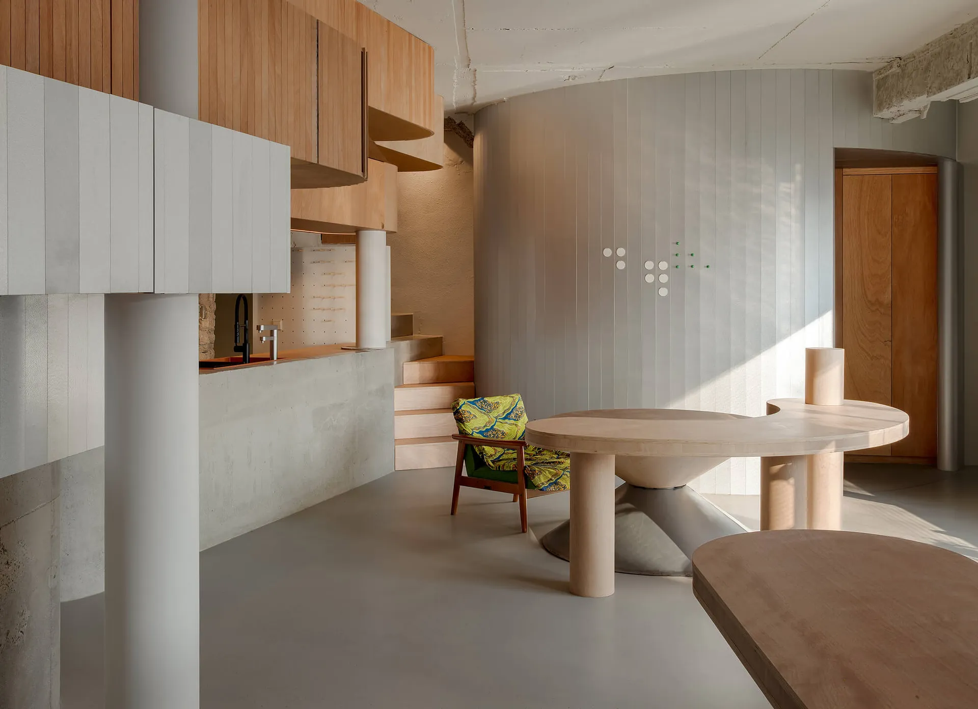 A well-lit living room with a dining table, kitchen area, and wooden decor, surrounded by natural light from the windows