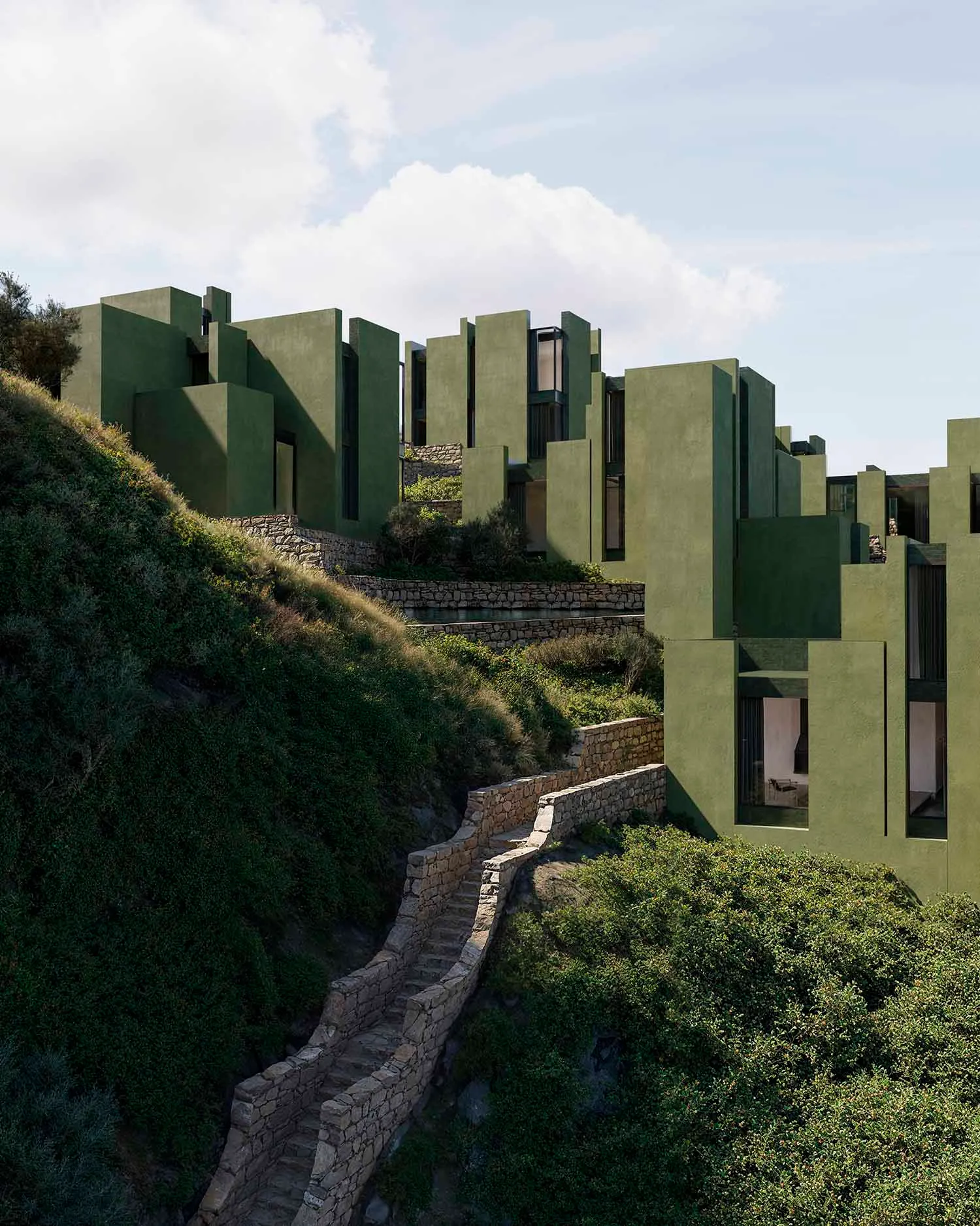 Modern building with a green exterior, surrounded by a lush hillside, featuring large windows for natural light and a serene atmosphere