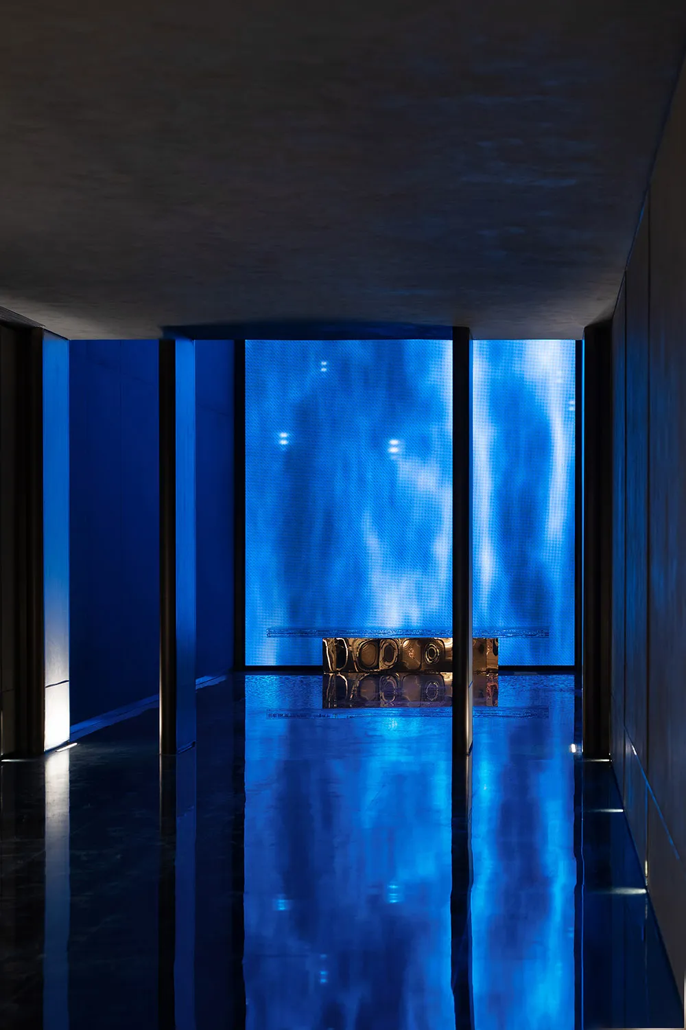 Blue-lit living room with a blue-tinted glass door, blue walls, and a couch in a modern and contemporary space