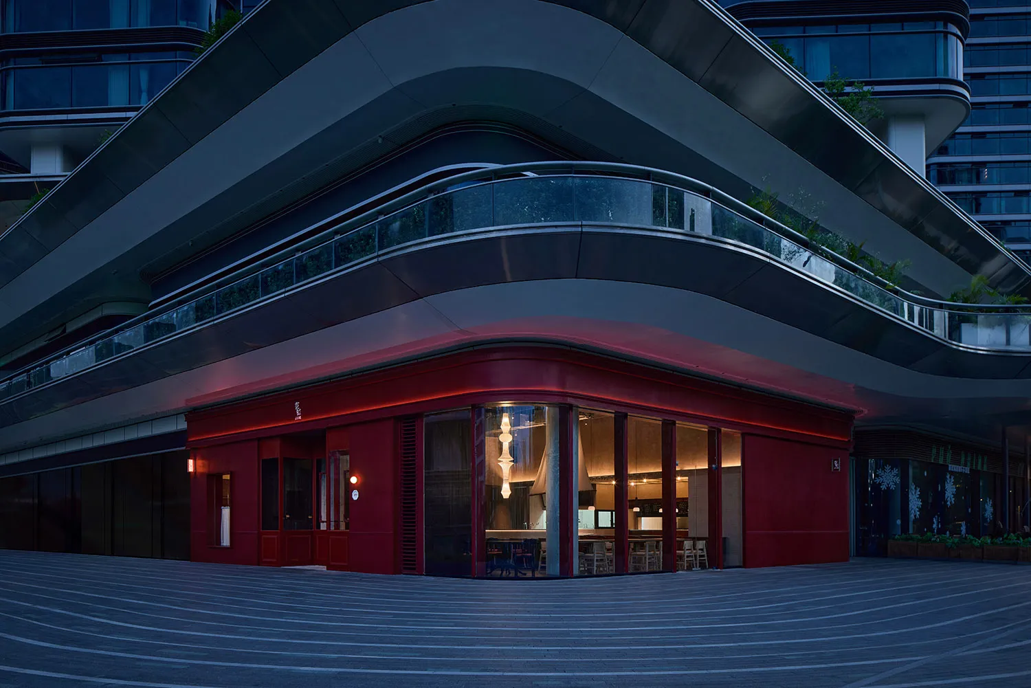 A modern restaurant with a red brick facade, featuring a large window and a cozy interior with chairs and dining tables