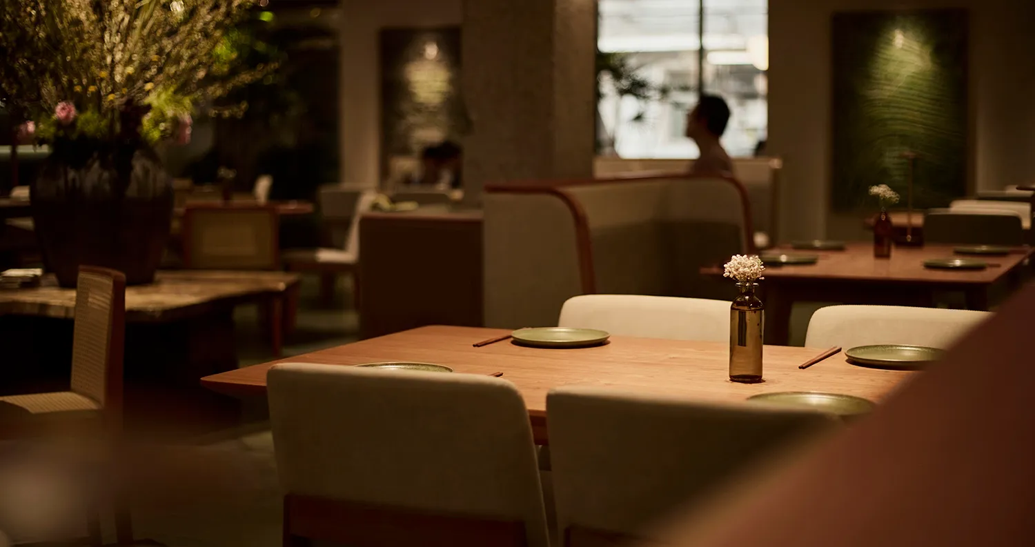 A calm and inviting restaurant with a wooden table and chairs, set with plates and a vase, in an empty space