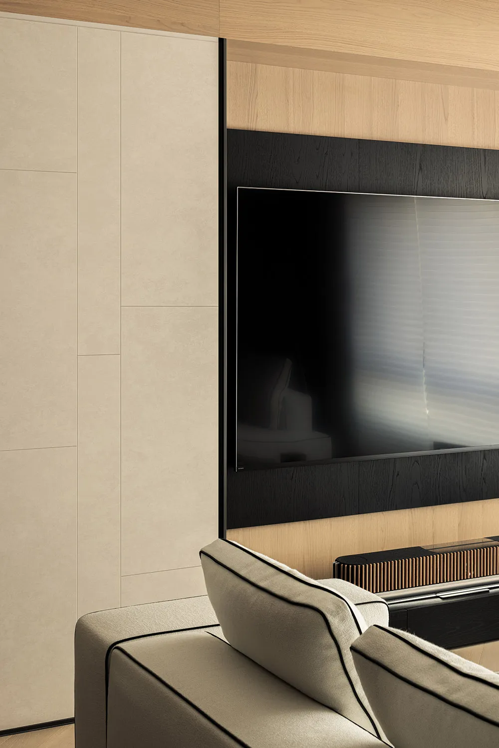 Modern living room sofa with beige upholstery facing a wall unit featuring beige textured panels, light wood grain, and a black recessed TV niche.