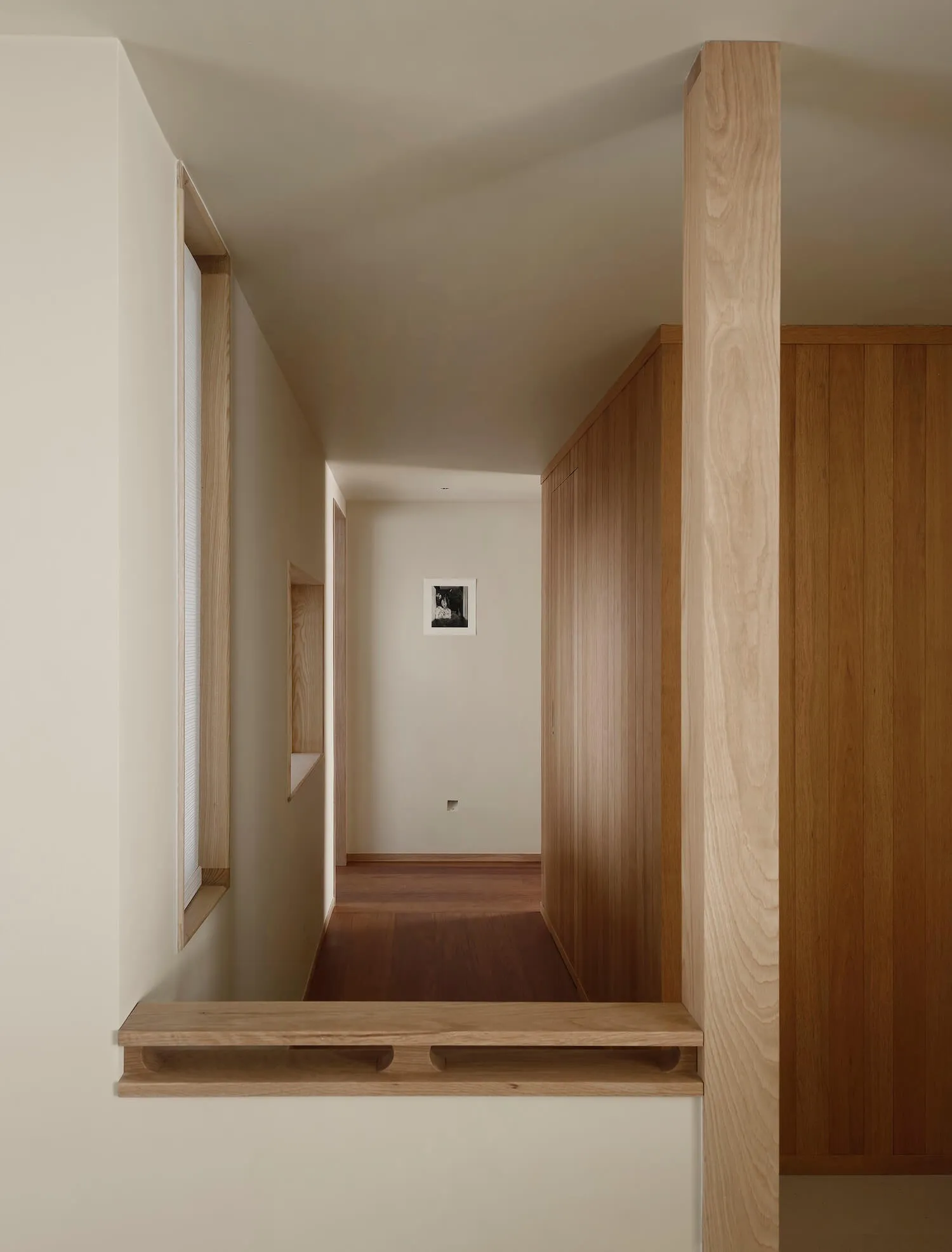 Narrow minimalist hallway featuring light oak wood paneling, built-in floating shelves, and a warm wood floor.