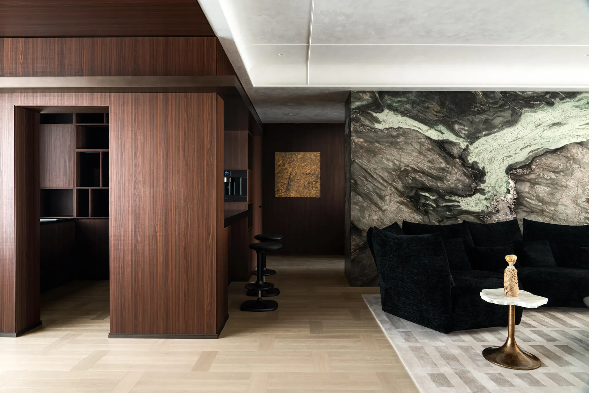Modern luxury living room featuring dark walnut wood cabinetry, a large green marble feature wall, black velvet modular sofa, and light herringbone wood flooring.