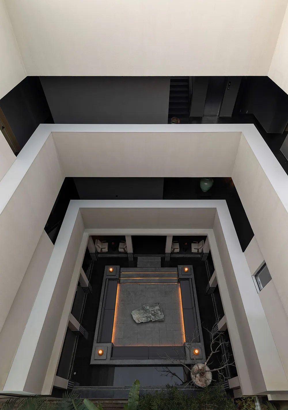 Top-down view of a modern architectural atrium with a sunken stone courtyard, recessed lighting, and surrounding white and dark grey walls.