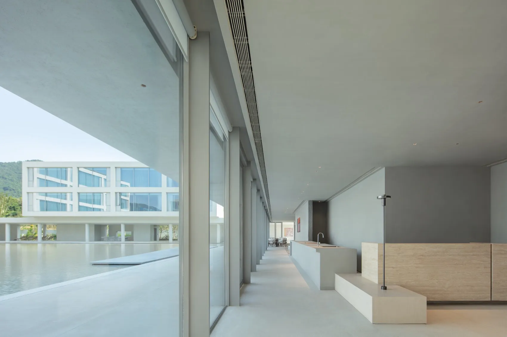 Modern minimalist indoor corridor overlooking a large reflecting pool with concrete walls and travertine accents