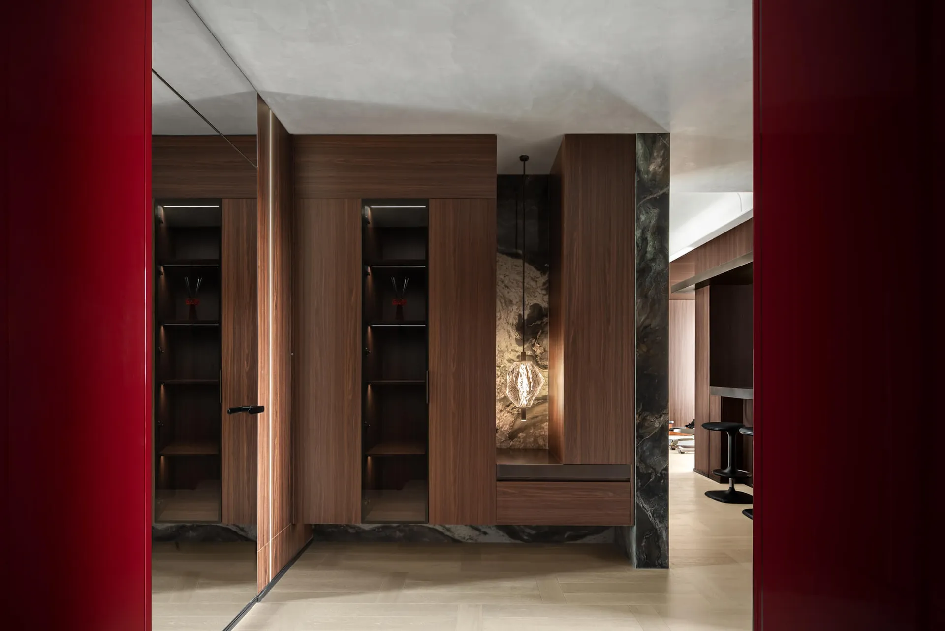 Modern luxury entryway featuring rich walnut built-in cabinetry, dark marble accents, glossy red lacquer doors, and a hand-blown glass pendant light.