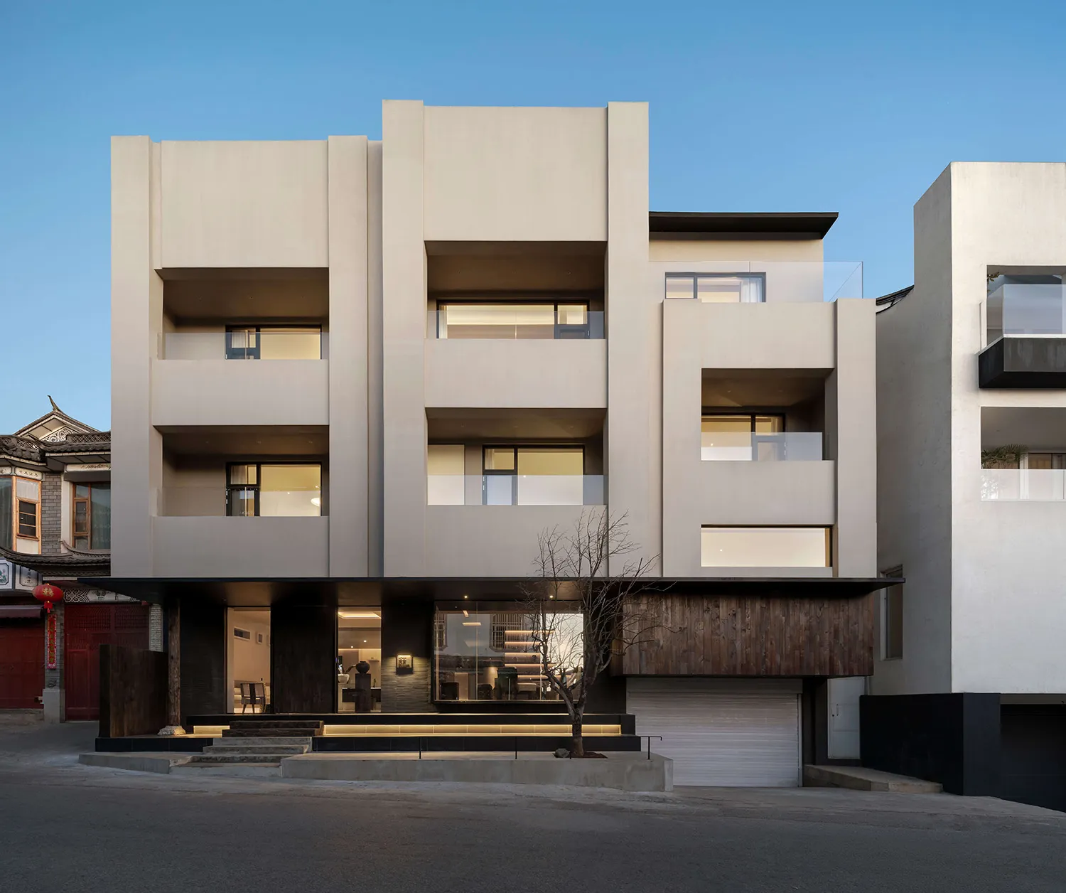Front elevation of a modern multi-level concrete villa with dark wood cladding, integrated lighting, and geometric balconies at twilight.