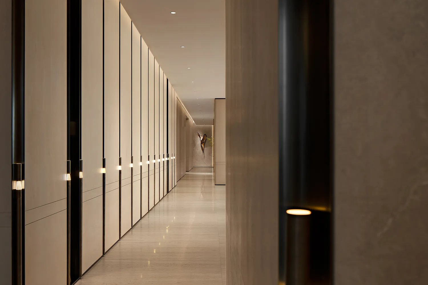 Long modern hallway featuring floor-to-ceiling light wood paneling with integrated vertical LED lighting and polished stone flooring.