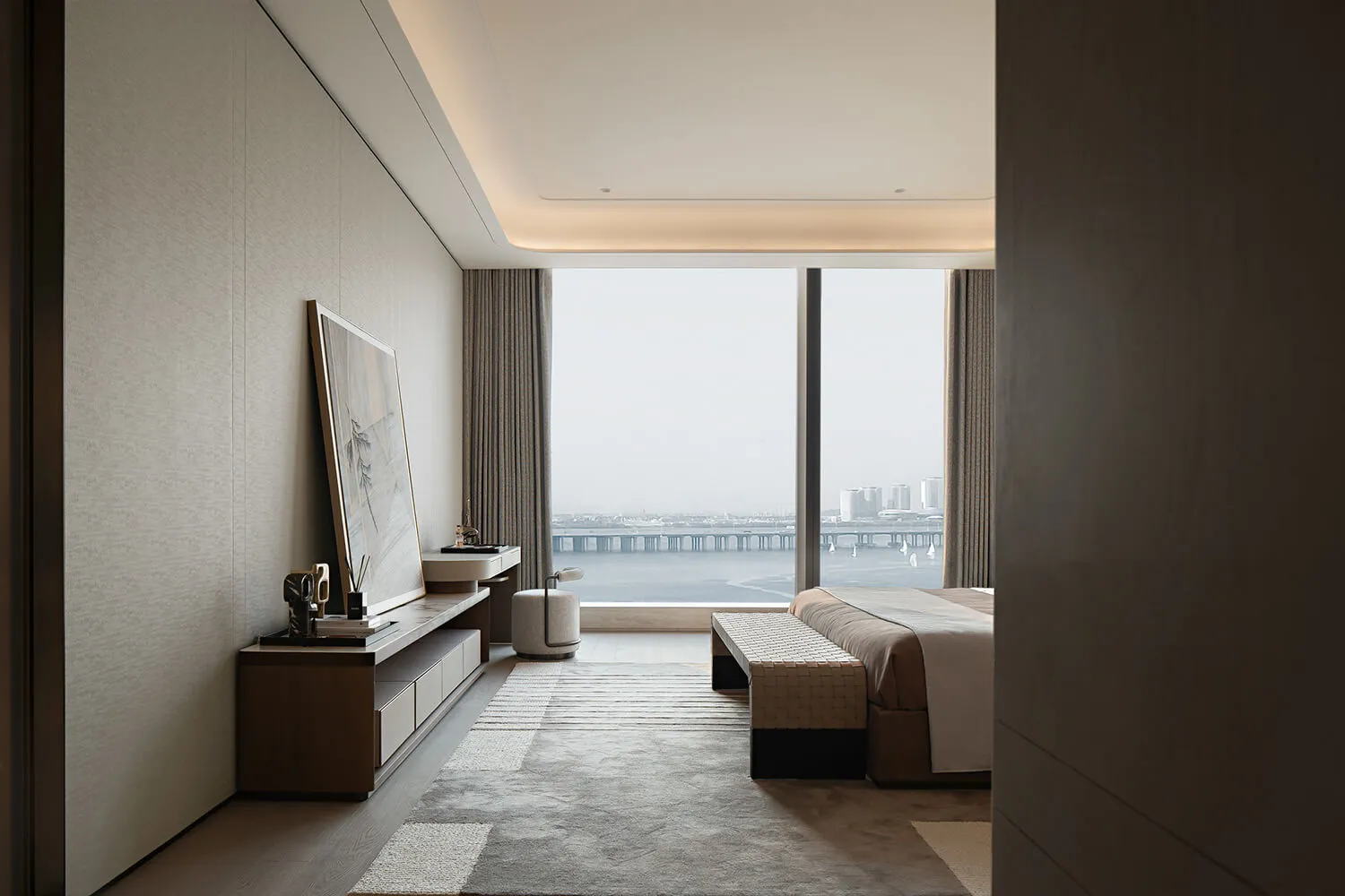 Modern luxury bedroom interior featuring a large harbor view window, walnut media console, textured area rug, and woven bench at the foot of the bed.