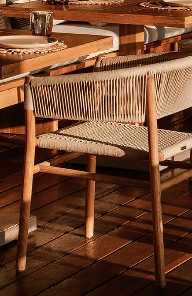 A wooden dining chair with beige rope weaving on the backrest and seat, placed on a dark wooden deck beside a solid wood dining table.