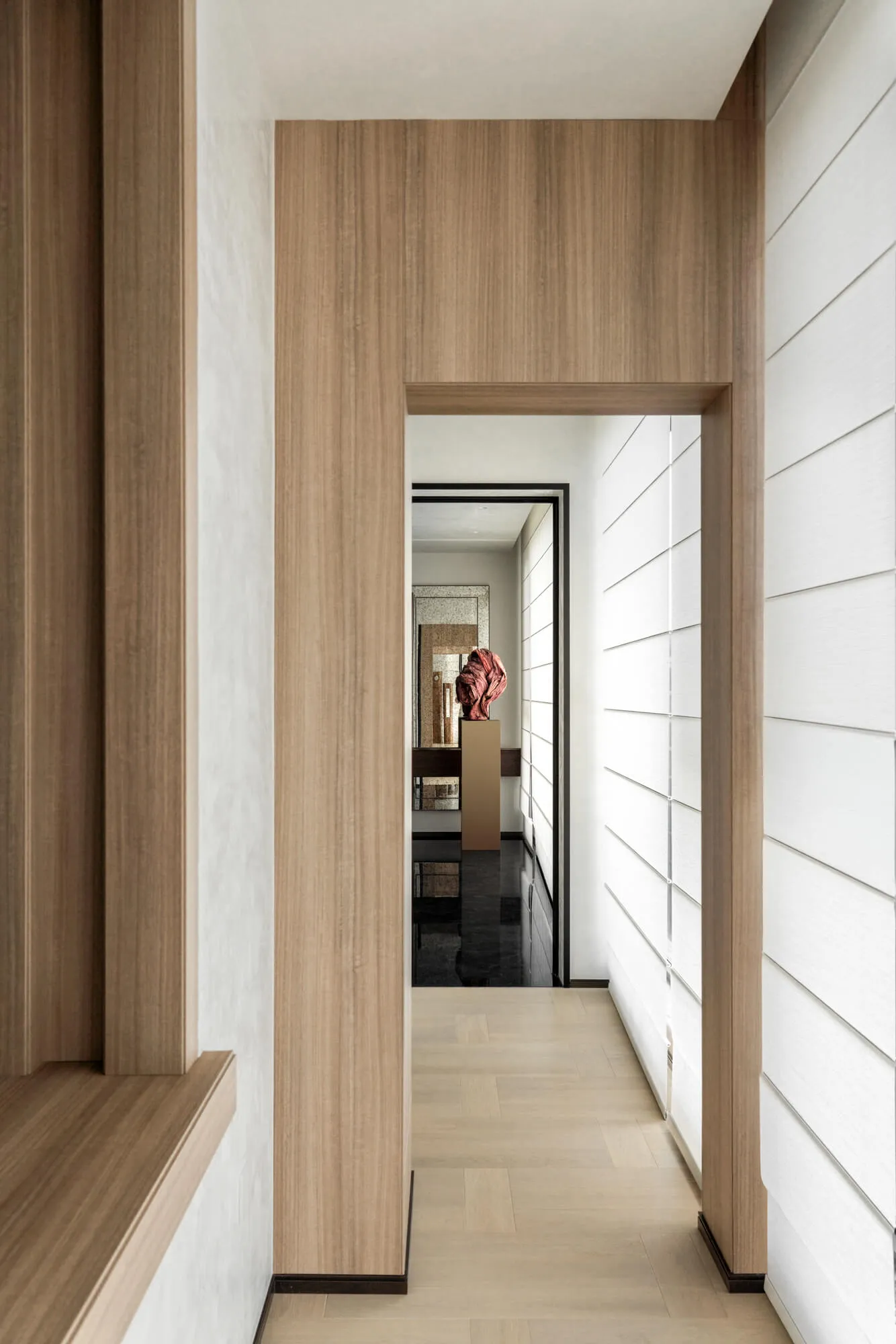 Modern minimalist hallway with light wood paneling, white textured walls, and a red stone sculpture displayed on a pedestal at the end of the corridor.