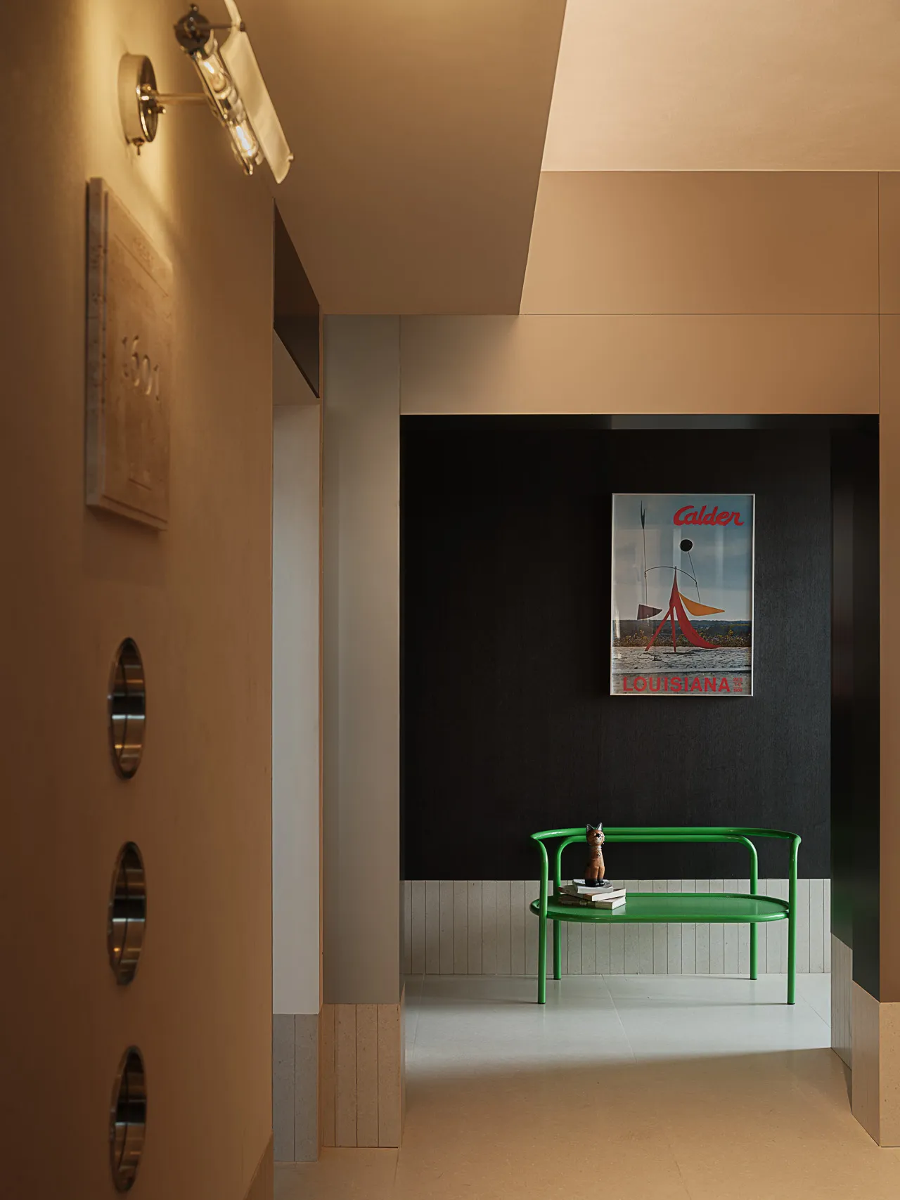 Modern minimalist entryway featuring a bright green metal bench, Alexander Calder Louisiana poster, warm wall sconce, and two-tone beige and dark grey walls with wood accents.
