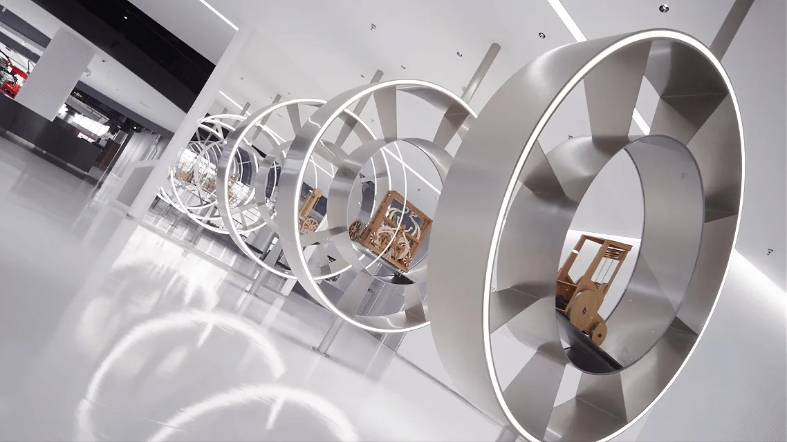 Large-scale stainless steel circular sculptures arranged in a receding tunnel formation inside a modern white exhibition space with reflective floors.
