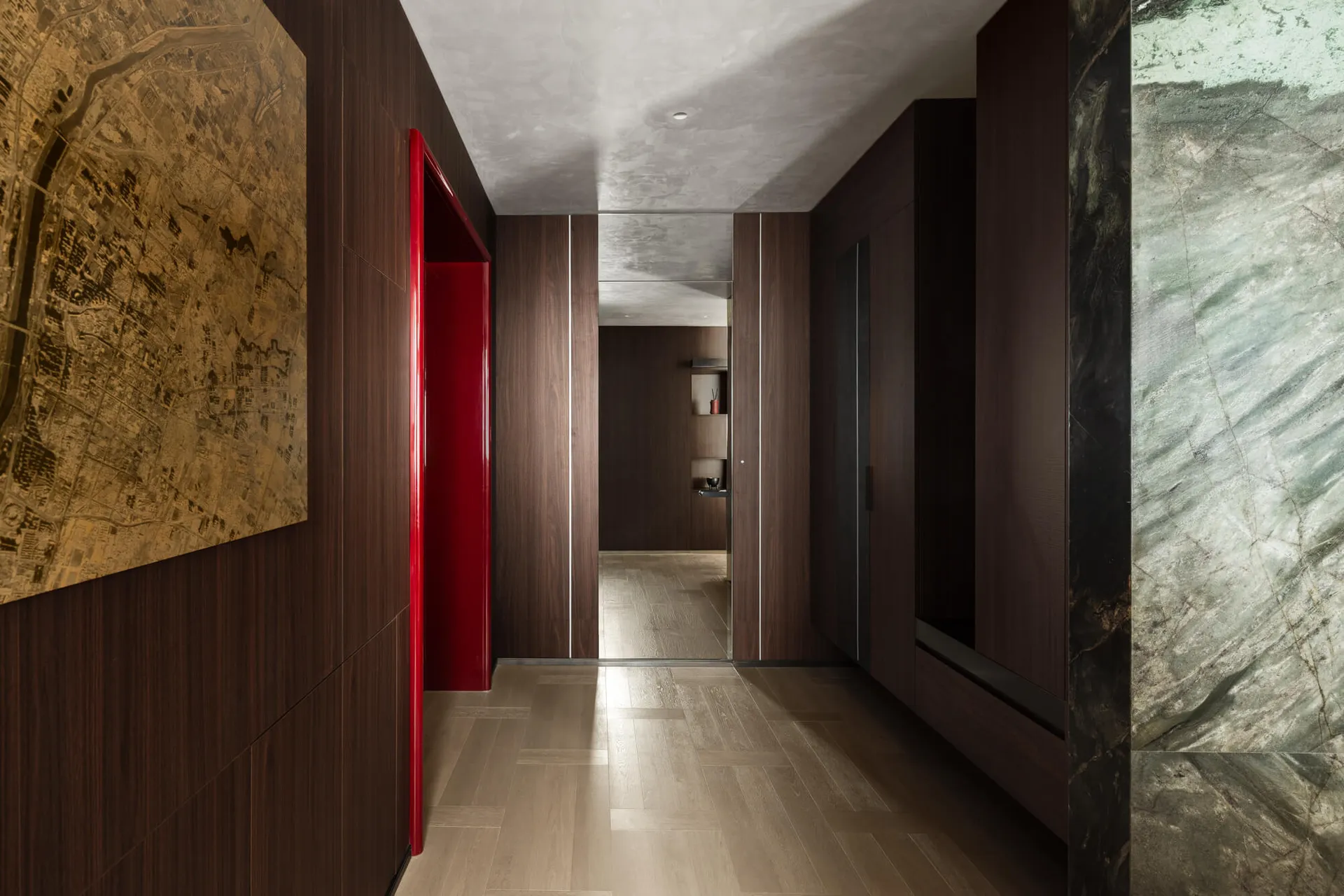 Modern luxury hallway with dark walnut wood walls, a glossy red door, green marble feature wall, and large city map artwork.