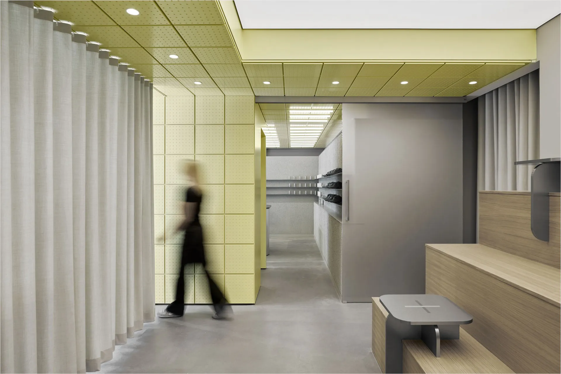 Modern shoe store interior with lime green perforated acoustic wall panels, white curtains, wooden bench, grey stool, and recessed ceiling lighting.