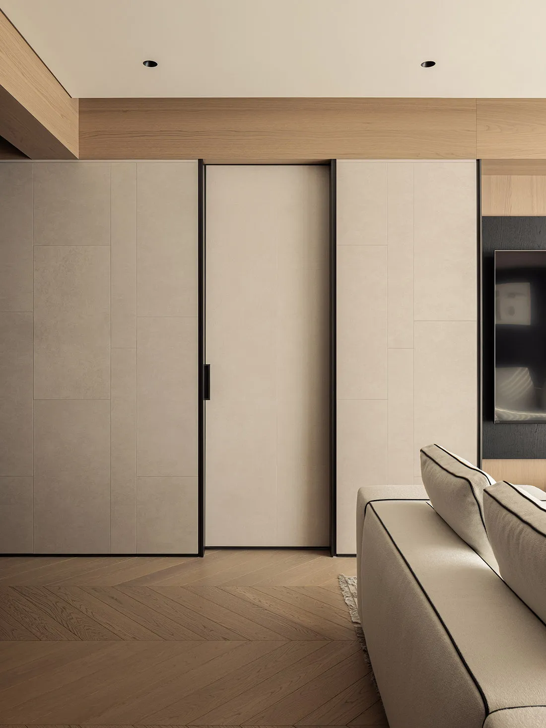 Modern minimalist living room featuring beige built-in cabinetry with black sliding door, light oak herringbone wood floor, and a portion of a neutral sofa with black piping.