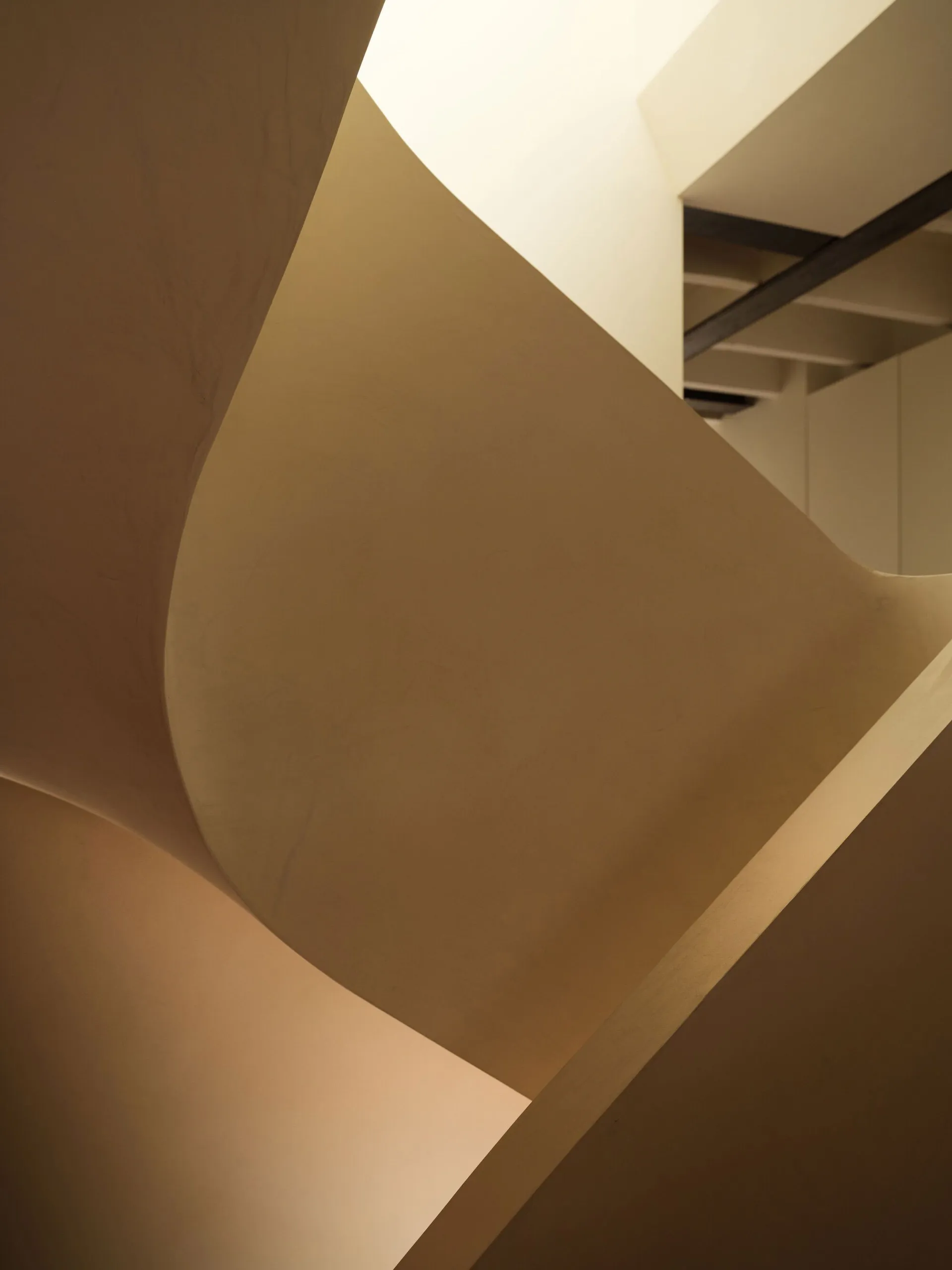 Close-up view of a sculptural curved plaster staircase with smooth organic forms and warm neutral tones.