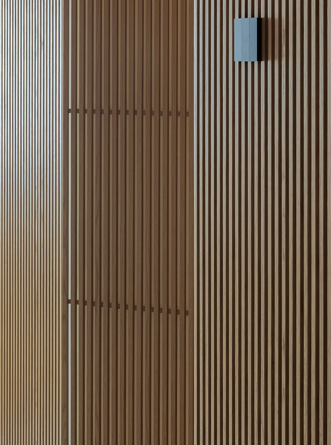 Close-up of a vertical oak wood slat wall featuring two horizontal bands of darker joinery and a modern rectangular blue wall sconce mounted on the upper right.