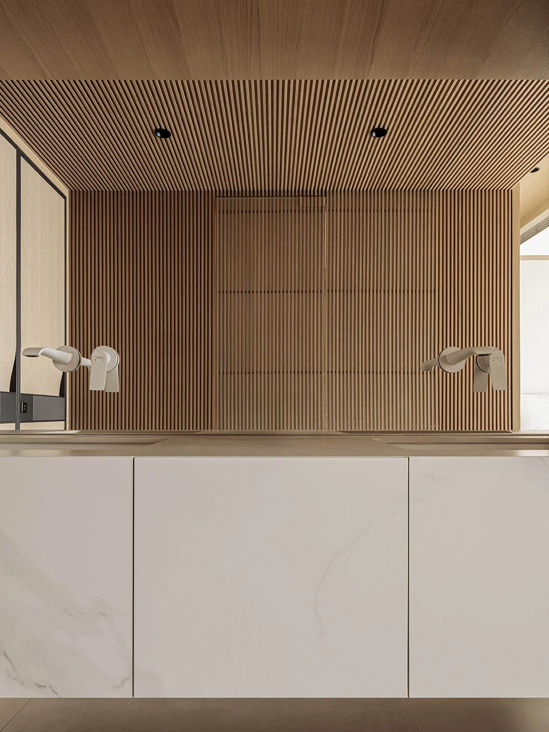 Modern minimalist bathroom vanity with white marble countertop and cabinetry, set against a vertical wood slat accent wall and matching slatted ceiling with recessed lighting.