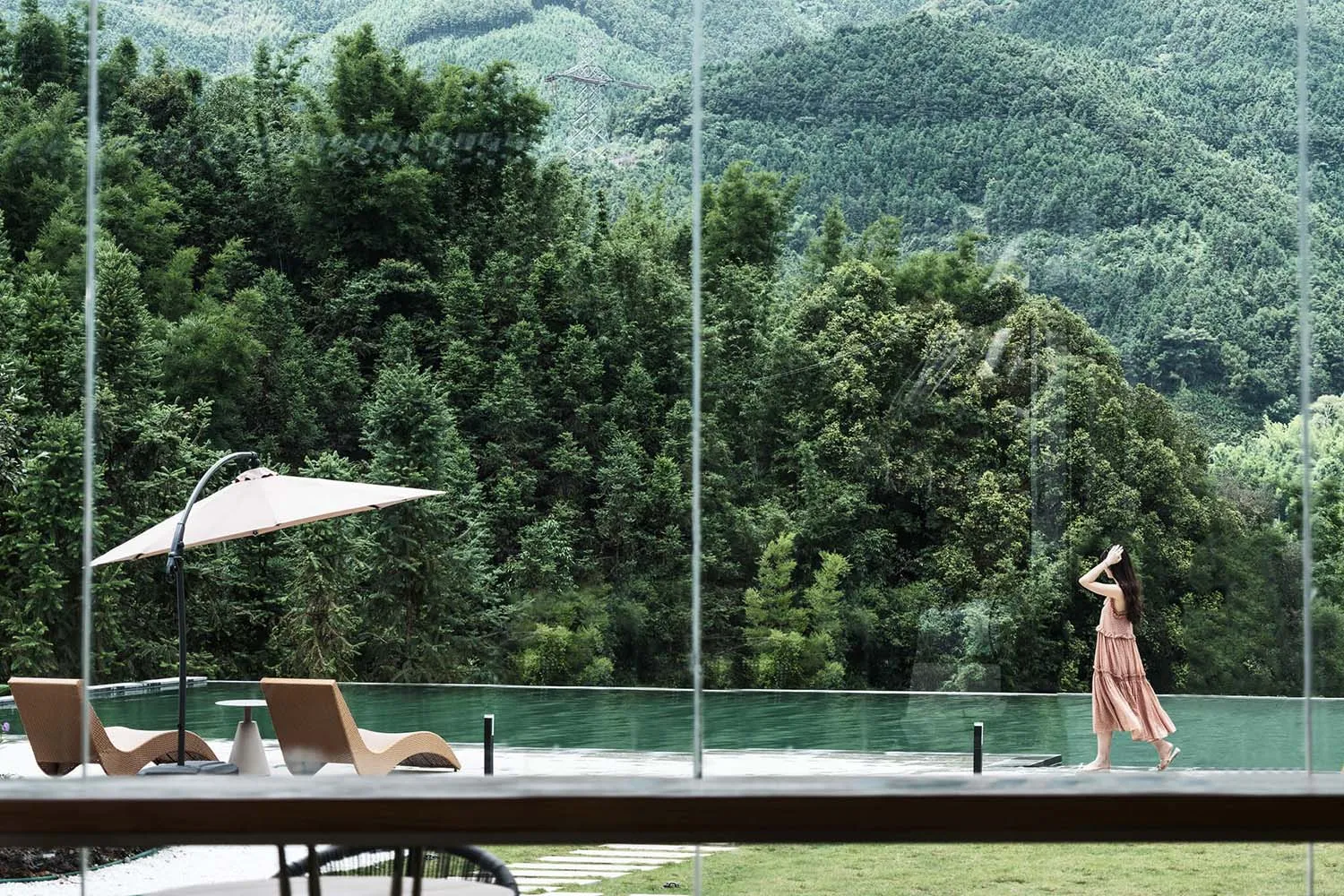 Modern infinity pool with wooden lounge chairs and a large umbrella, set against a dramatic backdrop of dense green mountains and forest in Taiwan.