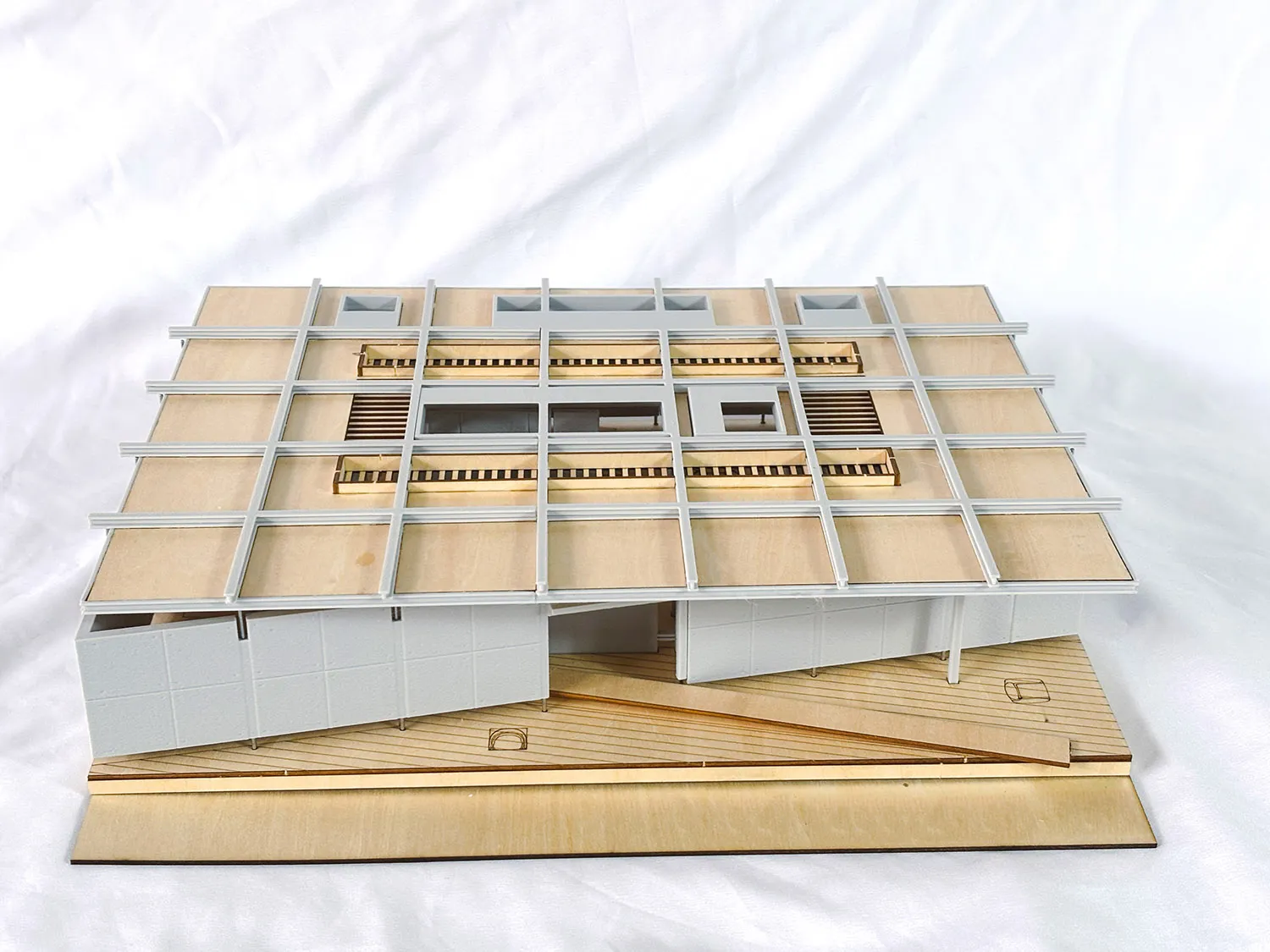 Architectural scale model of a modern house featuring a white grid facade, wooden structural elements, and an elevated wooden deck base.