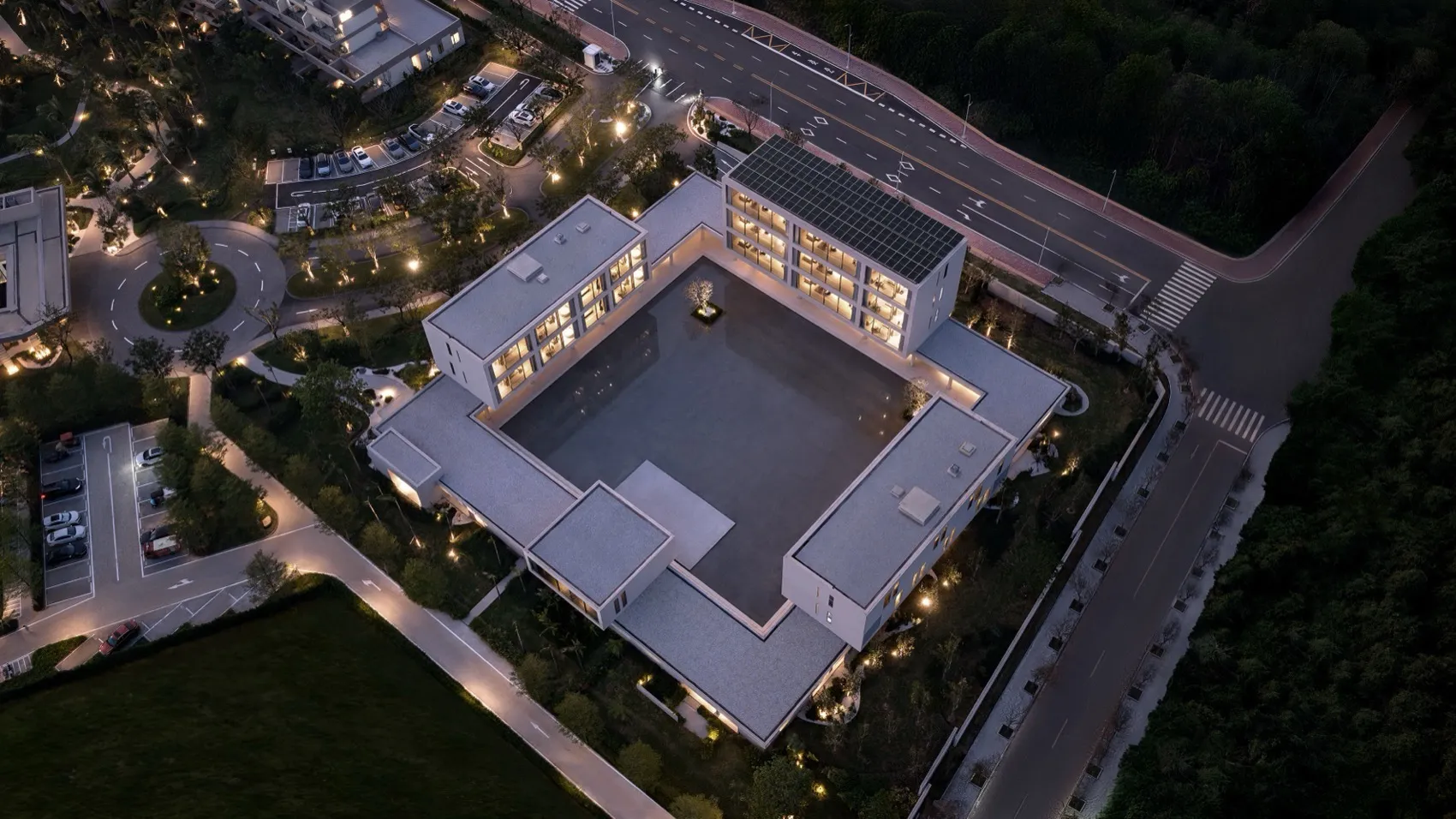 航拍夜景：現代U型混凝土別墅擁有大型中央中庭，周圍環繞景觀綠地與道路。