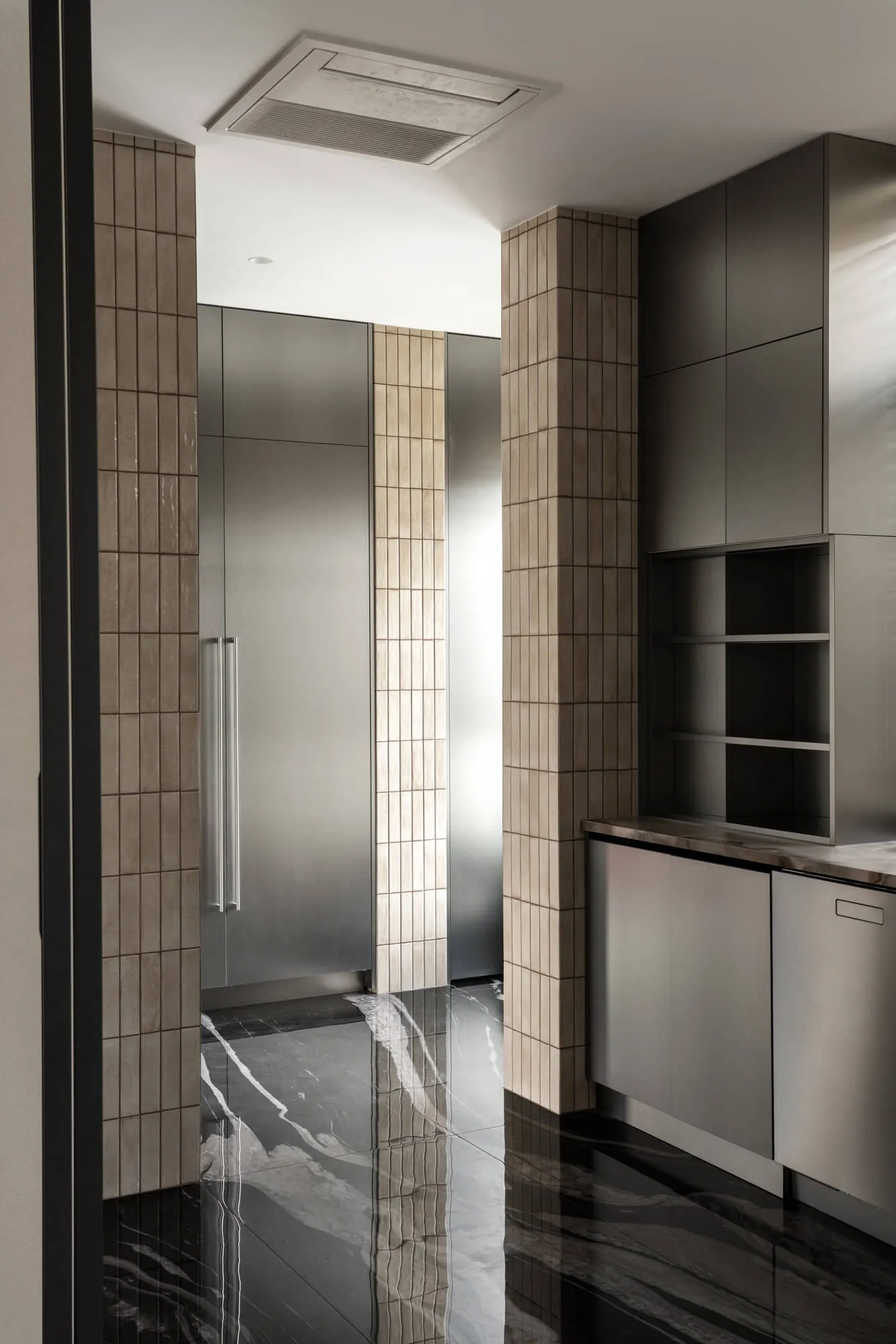 Modern minimalist kitchen corner featuring black marble flooring and walls with vertical beige tiles, stainless steel tall cabinets, and open shelving under dramatic overhead lighting.