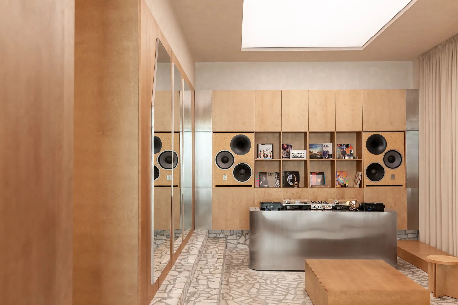 Modern music room with light birch plywood walls, built-in speakers, record collection, and a curved stainless steel console in the center.